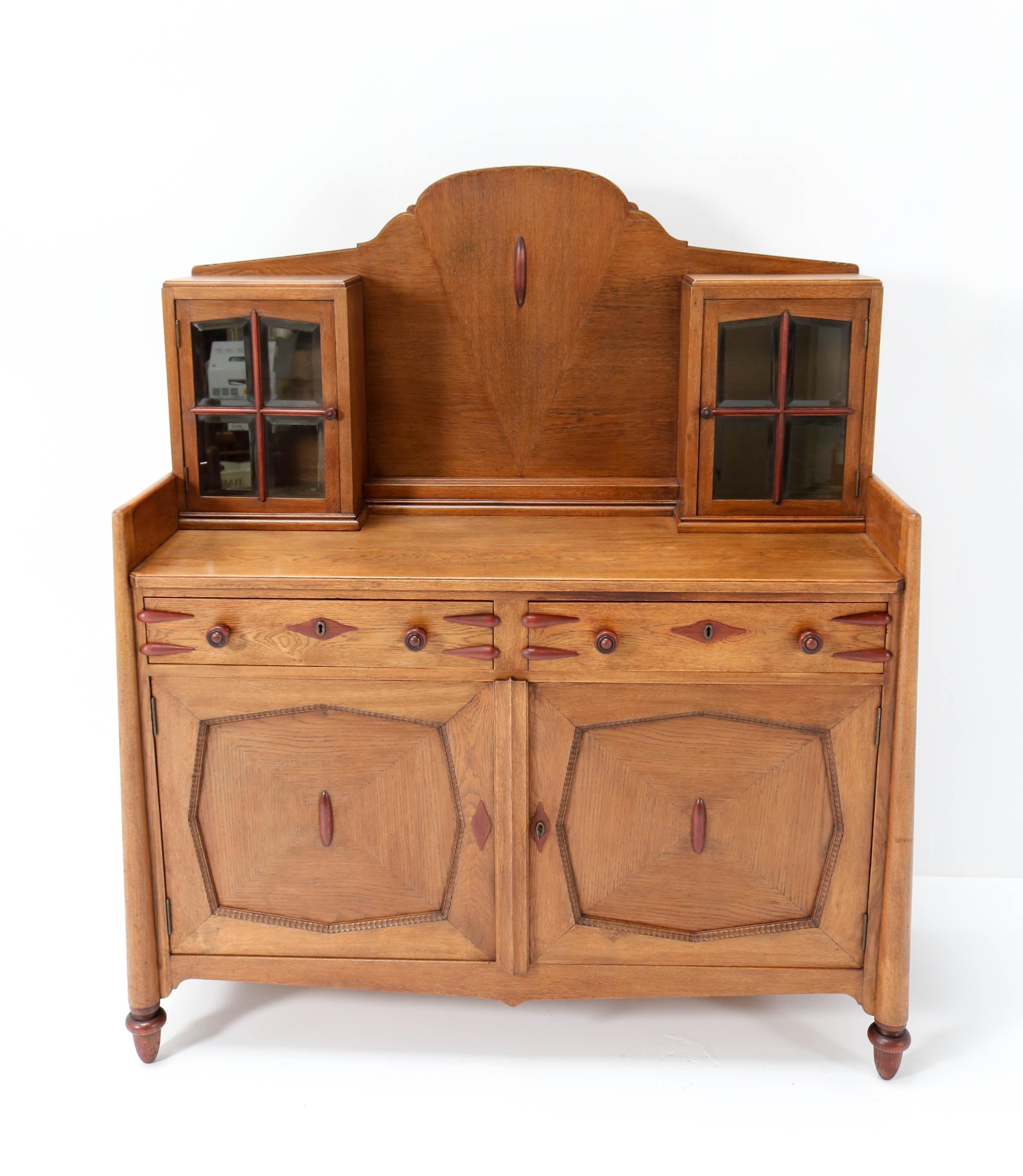 Magnificent and rare Art Deco Amsterdam School buffet or sideboard.
Design by Fa. Speelman Rotterdam.
Striking Dutch design from the 1920s.
Solid oak with mahogany knobs and details.
The top has original beveled glass in both doors.
In very