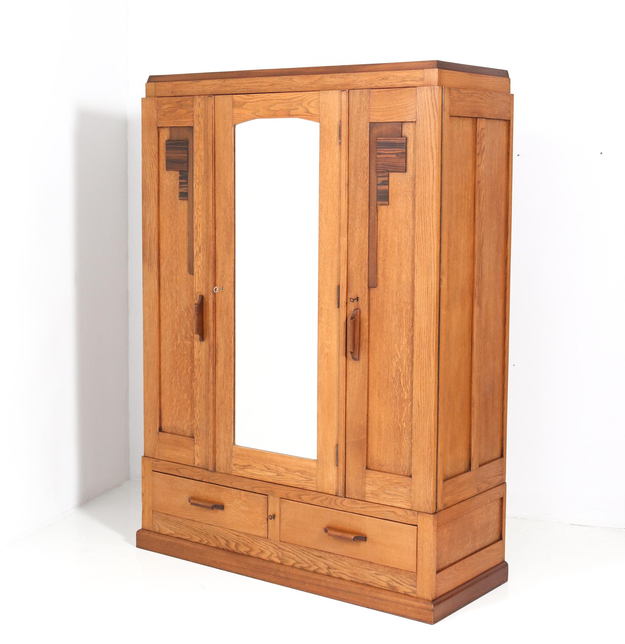 Stunning and rare Art Deco Amsterdamse School armoire or wardrobe.
Striking Dutch design from the 1920s.
Solid oak with original padouk handles and padouk and macassar lining.
The middle door has the original beveled glass mirror.
Three original