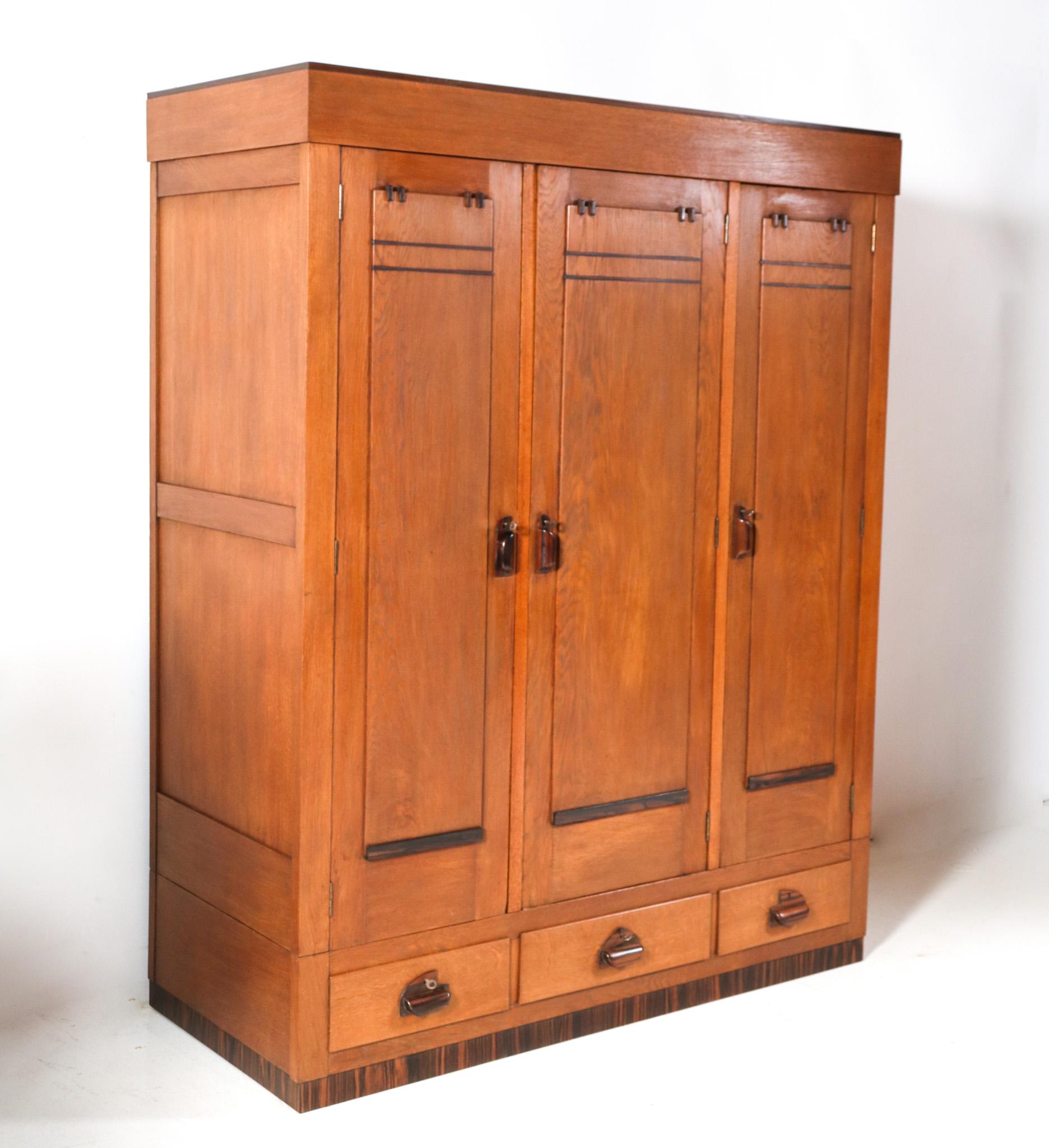 Magnificent and rare Art Deco Amsterdamse School three-doors armoire or wardrobe.
Striking Dutch design from the 1920s.
Solid oak base with solid macassar ebony handles on doors and drawers.
Behind the left door and right door, six original solid
