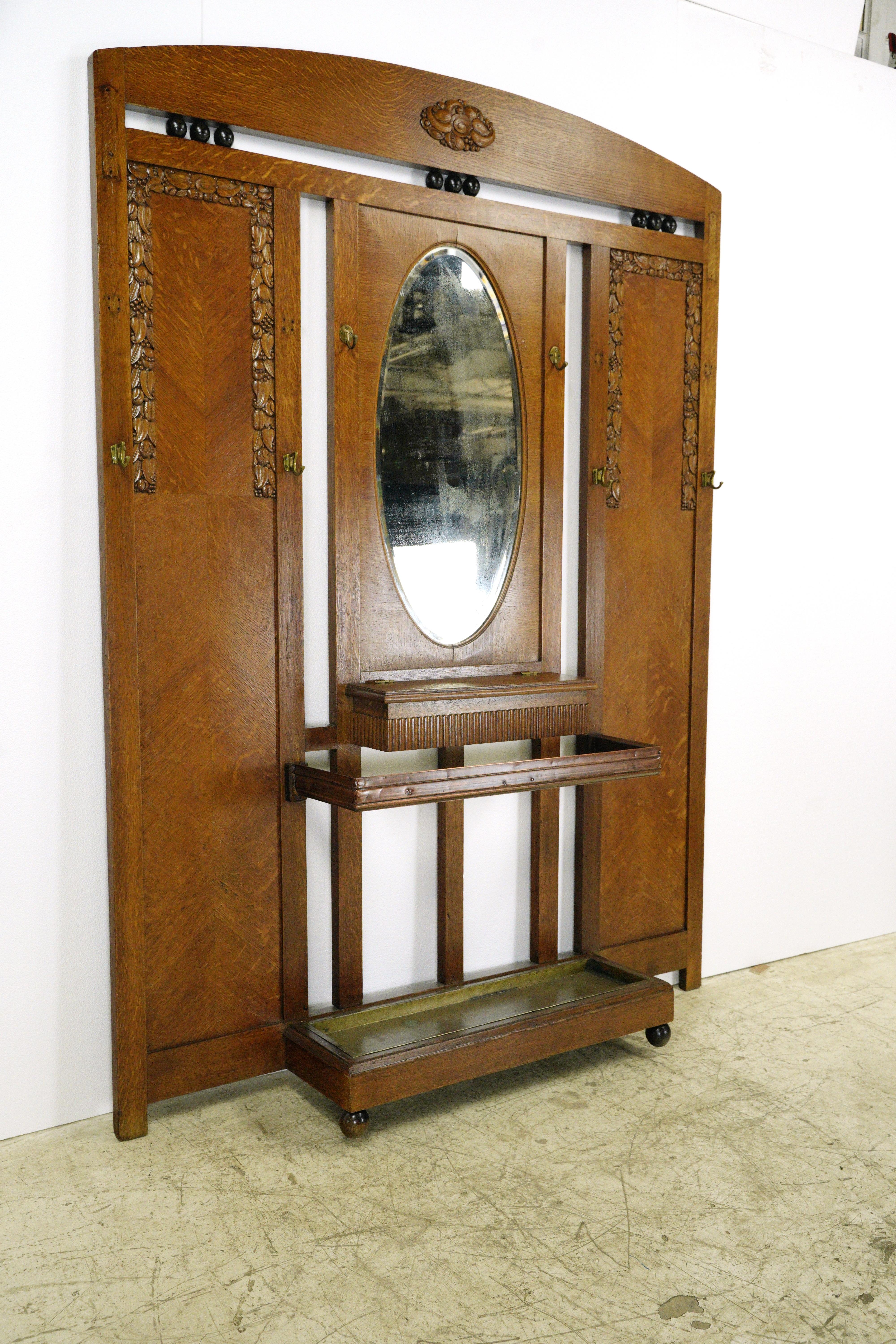 Art Deco style oak hall tree with an oval beveled mirror, carved decorative details and a bottom umbrella stand from the 1930s. Good condition with appropriate wear from age. Some minor wood cracking around mirror. One available.  Please note, this