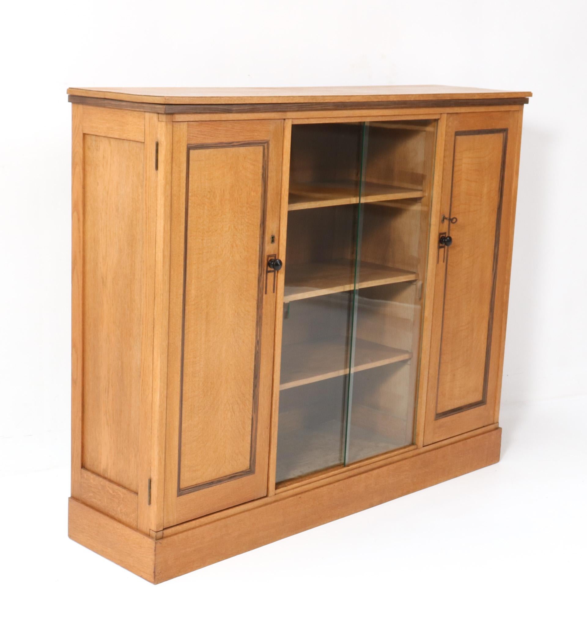 Stunning and rare Art Deco Modernist bookcase.
Striking Dutch design from the 1920s.
Solid oak bookcase with solid macassar ebony knobs on the left and right door.
The mid-section has two original glass sliding doors.
Nine original solid oak shelves
