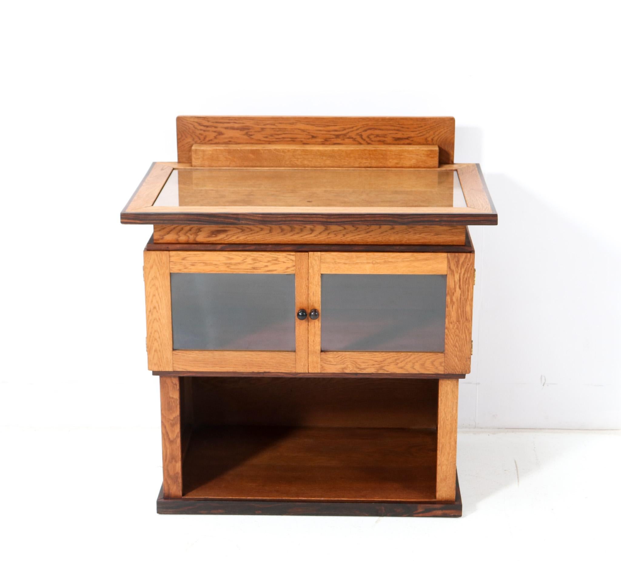 Stunning and rare Art Deco Modernist tea cabinet.
Design by P.E.L. Izeren for De Genneper Molen.
Solid oak with original oak veneered frame with original macassar ebony knobs on both doors.
Original glass top.
Purchased by the former owners in
