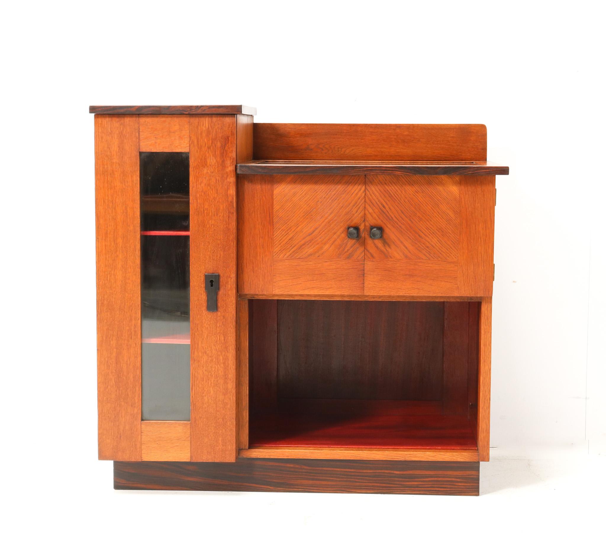 Stunning and rare Art Deco Modernist tea cabinet.
Design by P.E.L. Izeren for De Genneper Molen.
Striking Dutch design from the 1920s.
Solid oak with original oak veneer base with two original solid macassar ebony knobs on the two small doors.
Two
