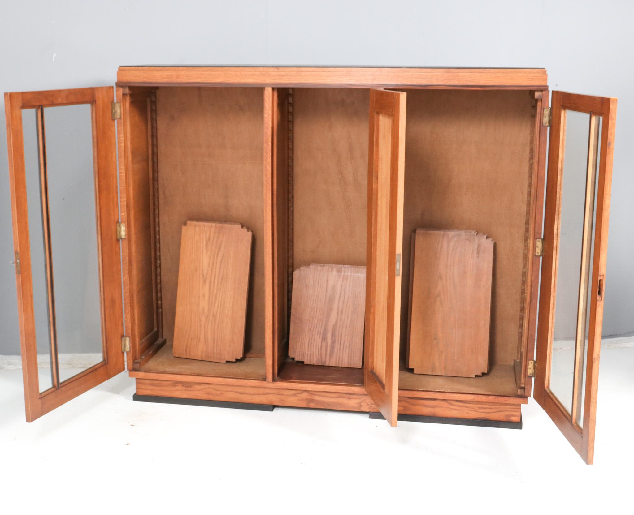 Stunning and rare Art Deco Modernist three-door bookcase.
Striking Dutch design from the 1920s.
Solid oak base with original veneered black lacquered top.
Nine original solid oak shelves, adjustable in height.
In very good original condition with