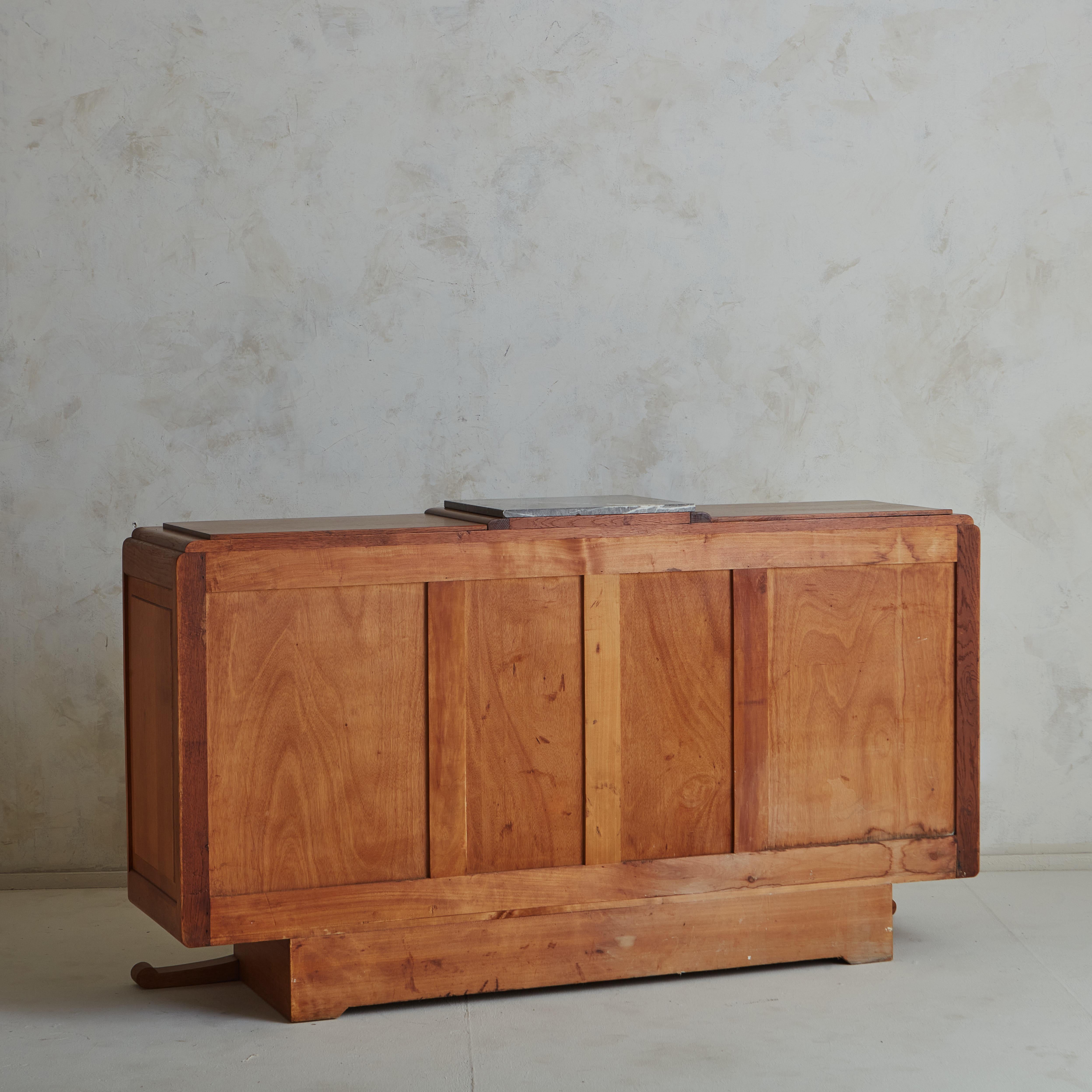 A Beautiful Art Decò 1930’s oak sideboard. This mesmerizing piece displays a huge amount of details, from the decorated foot and the marble top to the astonishing wood parquetry on the cabinet doors. 3 cabinet doors open to reveal interior storage.