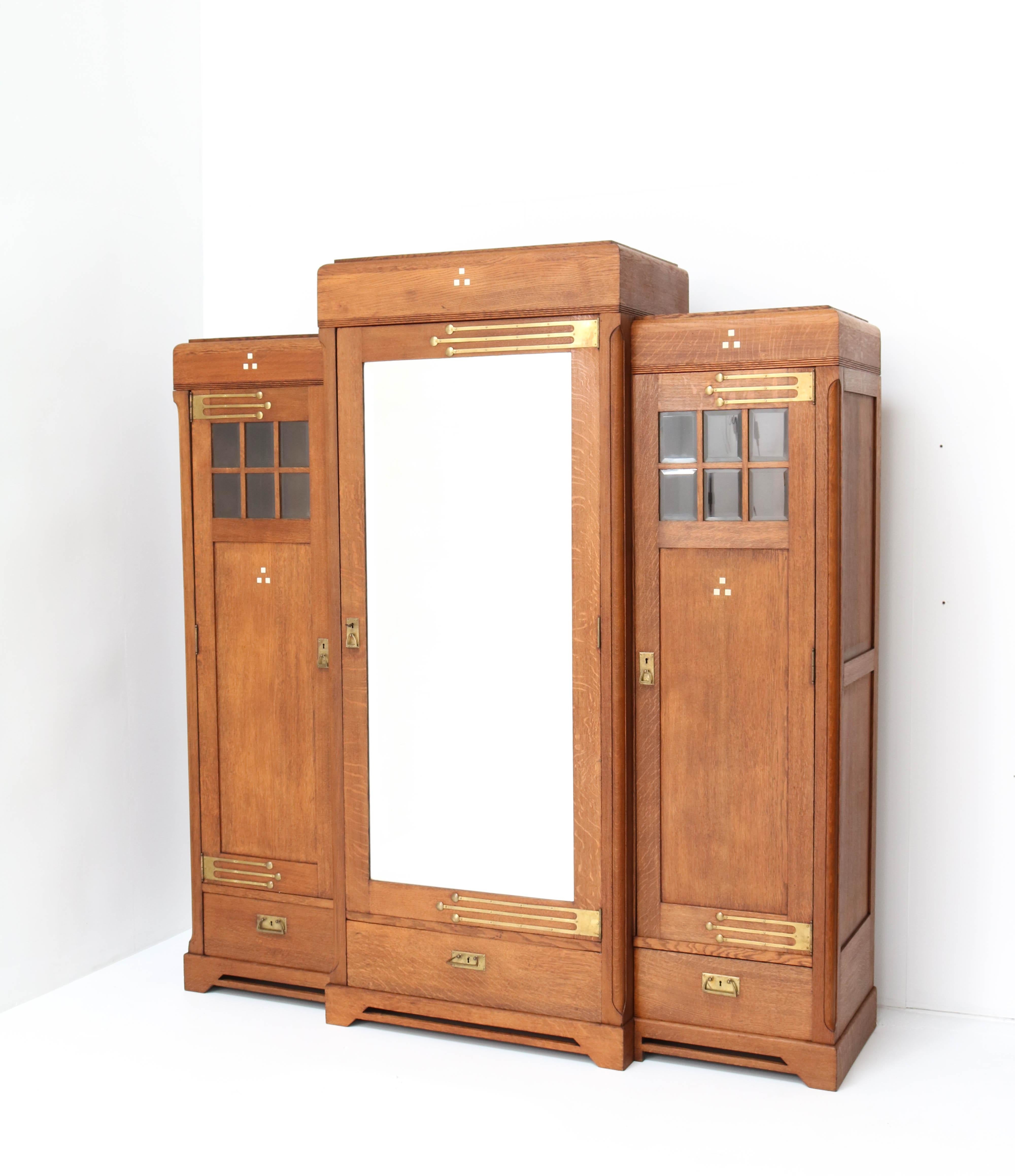 Magnificent and rare Art Nouveau Arts & Crafts armoire or wardrobe.
Striking Dutch design from the 1900s.
Solid oak with original solid brass hinges and handles.
All three doors have the original beveled glass and beveled glass mirror.
This