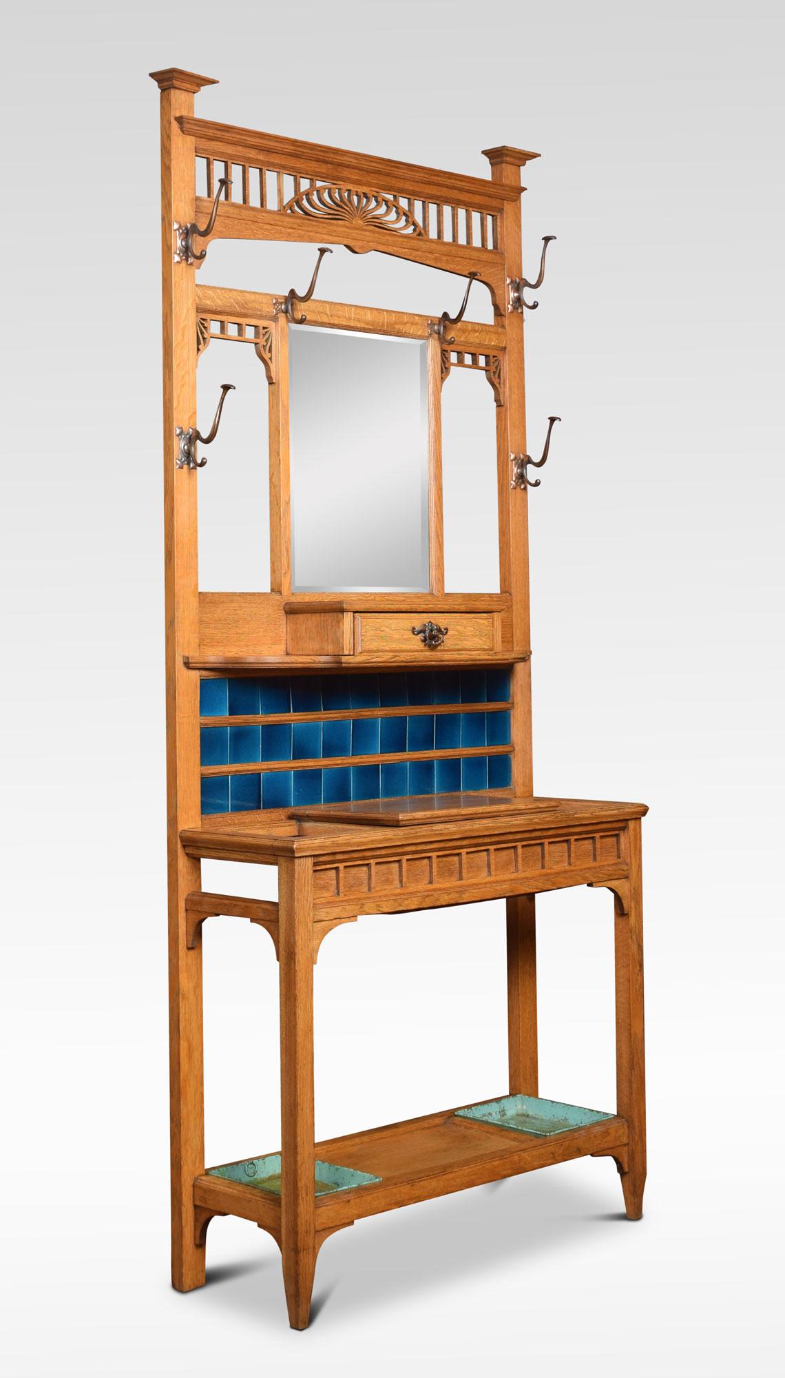 An early 20th century oak Arts & Crafts hall stand. The pierced top rail above the original rectangular mirrored plate and a shaped shelf. Fitted with a small drawer. The base section with tiled back and lift up glove box flanked by two stick