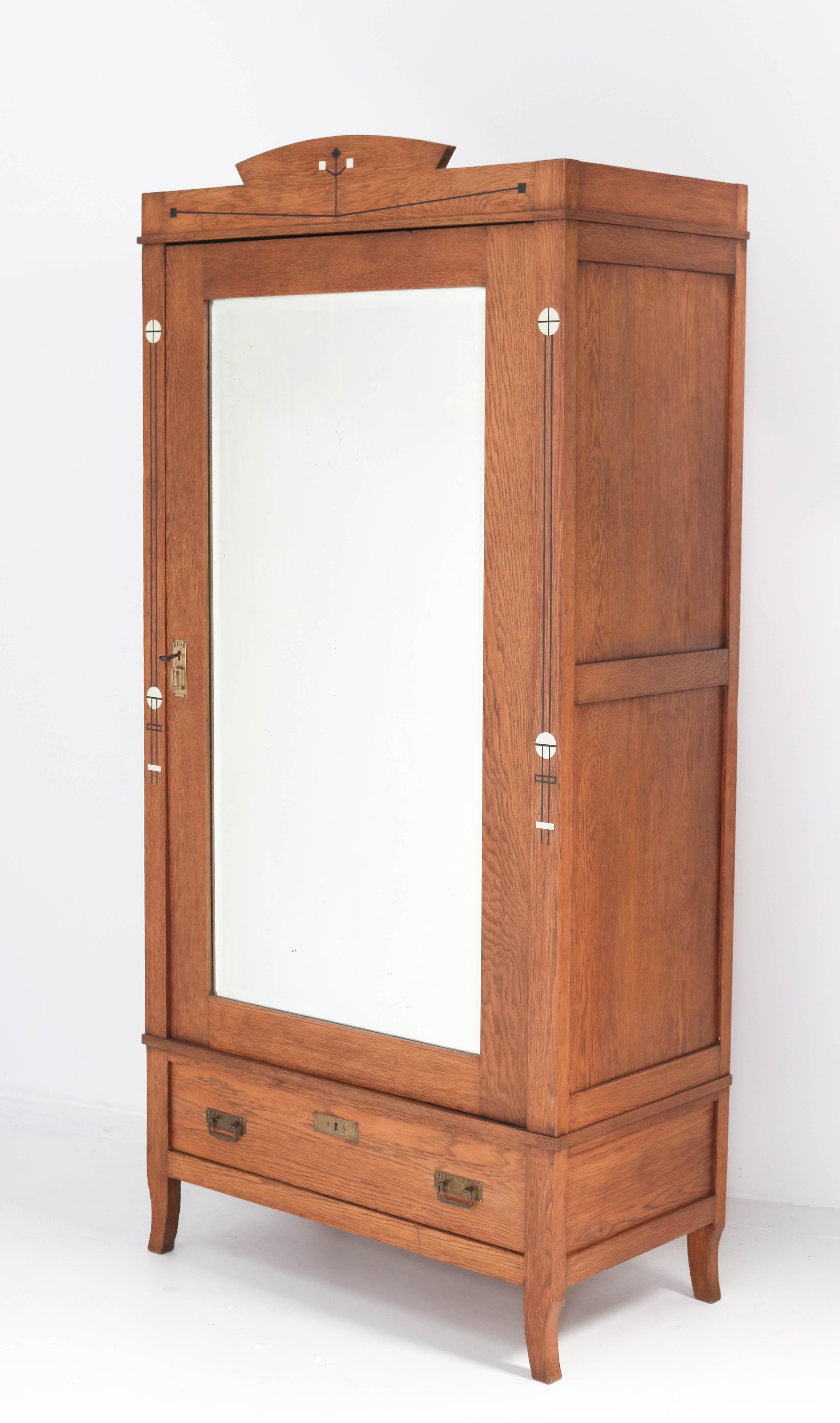 Wonderful and rare Arts & Crafts Art Nouveau armoire or wardrobe.
Striking Dutch design from the 1900s.
Solid oak with brass handles and original inlay.
The door has the original beveled mirror.
Three wooden shelves adjustable in height.
This