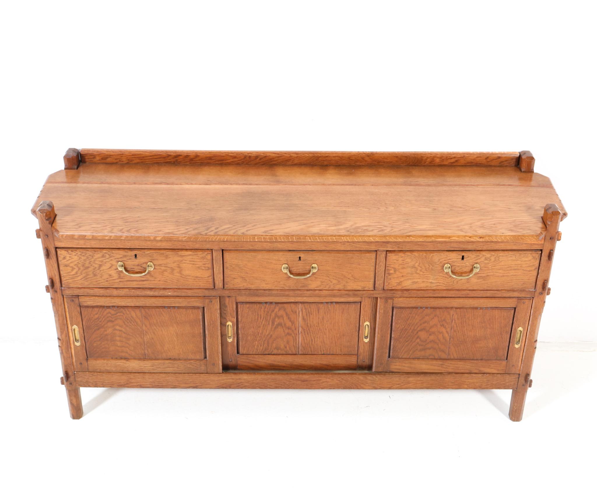 Magnificent and rare Arts & Crafts credenza or sideboard.
Design by Alexander J. Kropholler.
Striking Dutch design from the 1920s.
Solid oak with original brass handles on the three drawers and the three sliding doors.
This wonderful Arts &