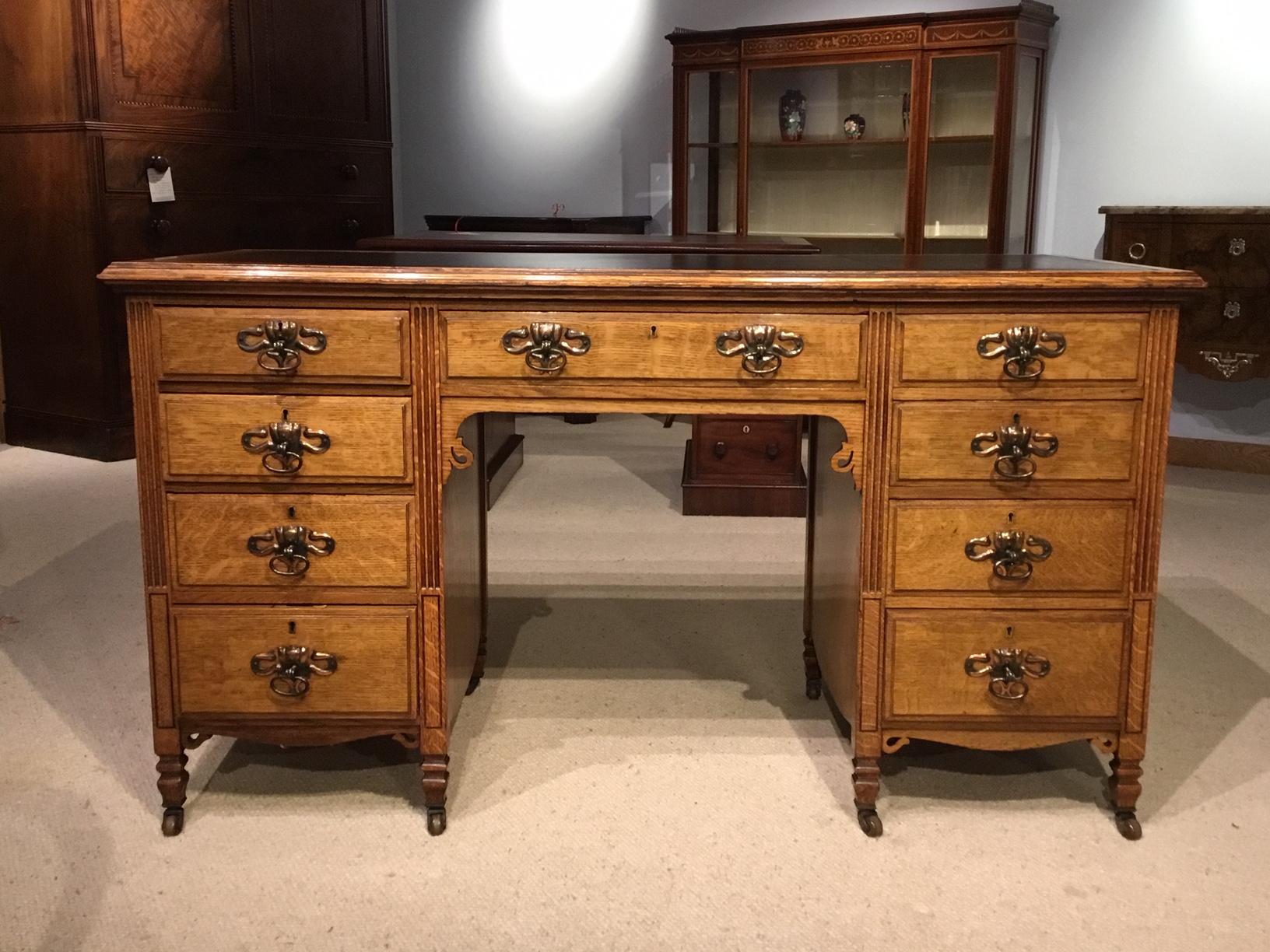 A quality oak Arts & Crafts period antique desk. Having a rectangular solid oak top with a black leather writing surface with gilt and black tooled detail. The front having an arrangement of nine rectangular drawers each with mahogany linings and