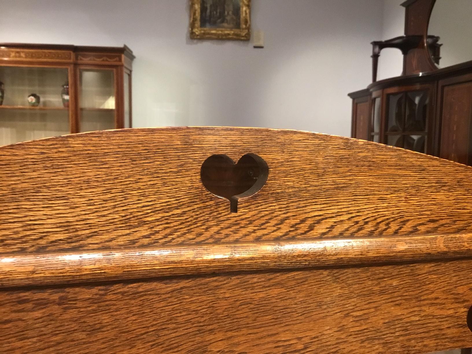 An oak Arts & Crafts period hall bench or umbrella stick stand. The back with three pierced heart shaped motifs typical of the designs of Liberty of London and having a shaped oak seat and open ends for storage of umbrellas/walking sticks etc.