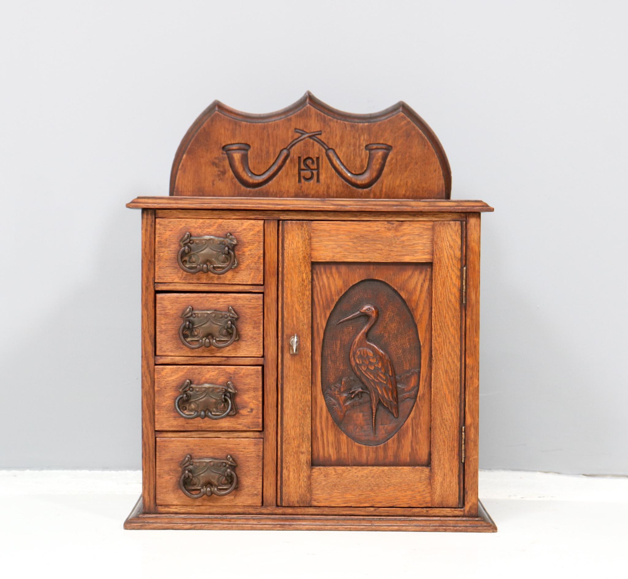 Stunning and rare Arts & Crafts wall cabinet.
Striking Dutch design from the 1900s.
Solid oak base with four original drawers with original patinated metal handles.
Hand-carved decorations of hunting horns and in the door a hand-carved decoration of