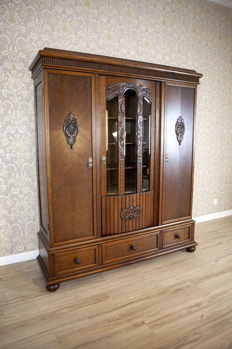 Libreria in Oak degli anni '30 in marrone

Un mobile a tre ante con tre cassetti nella parte inferiore. La facciata delle porte centrali è divisa e vetrata (con vetri originali) e riccamente decorata con intagli in legno, con motivi vegetali. Le