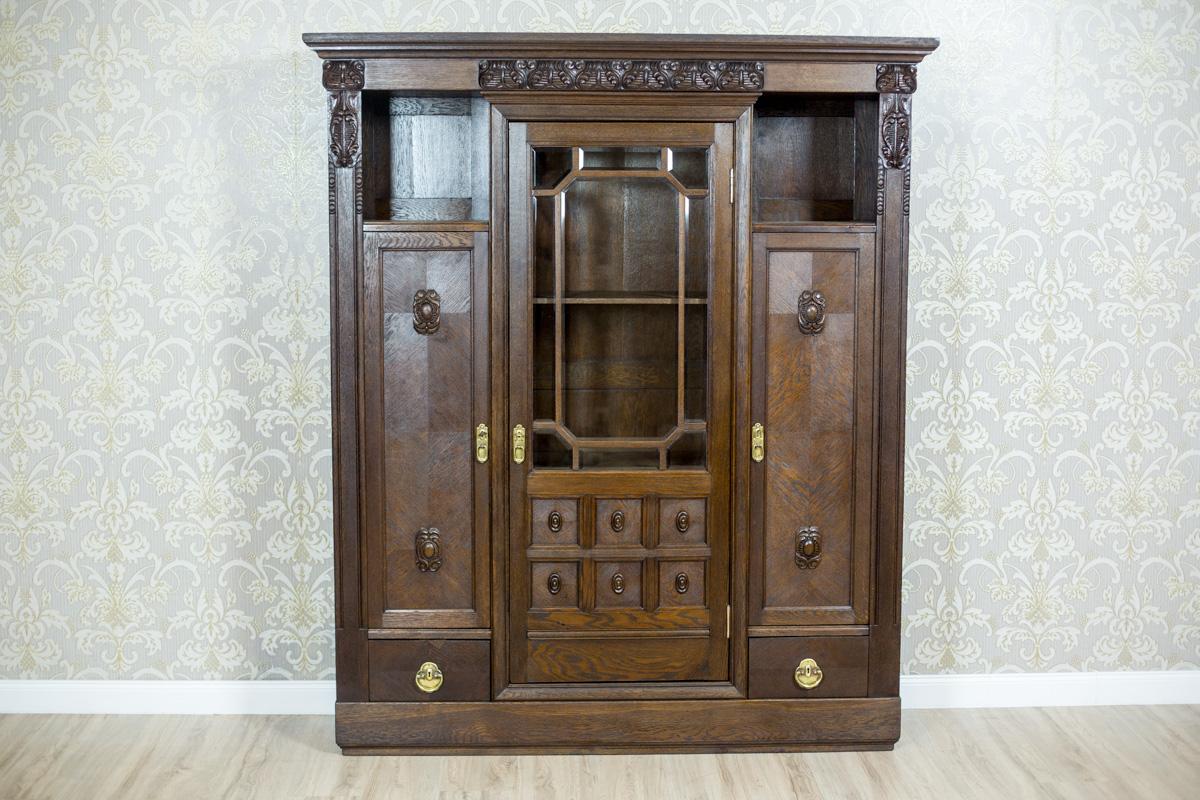 A piece of furniture made in wood and oaken face veneer, on a small cornice which ends with a profiled molding.
In the central section, there are glazed doors with crystal windows that are divided with bolections.
The outer doors of the bookcase