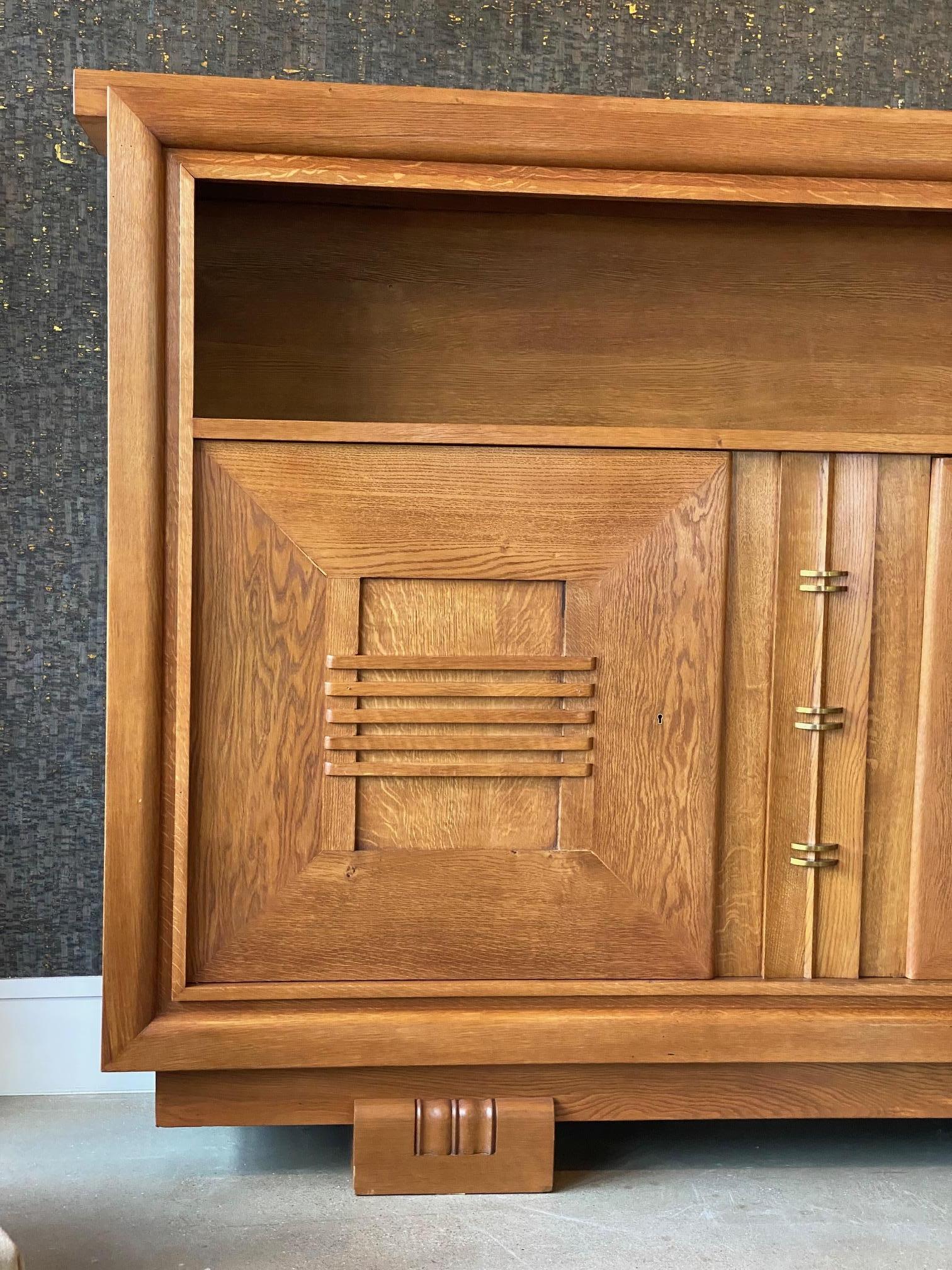 Uniquely scaled and handsome oak cabinet by Charles Dudouyt on solid block feet.  Two hinged doors on left and right side with open adjustable shelf interiors.  A center sliding panel conceals a narrow set of adjustable shelves in the center. 
