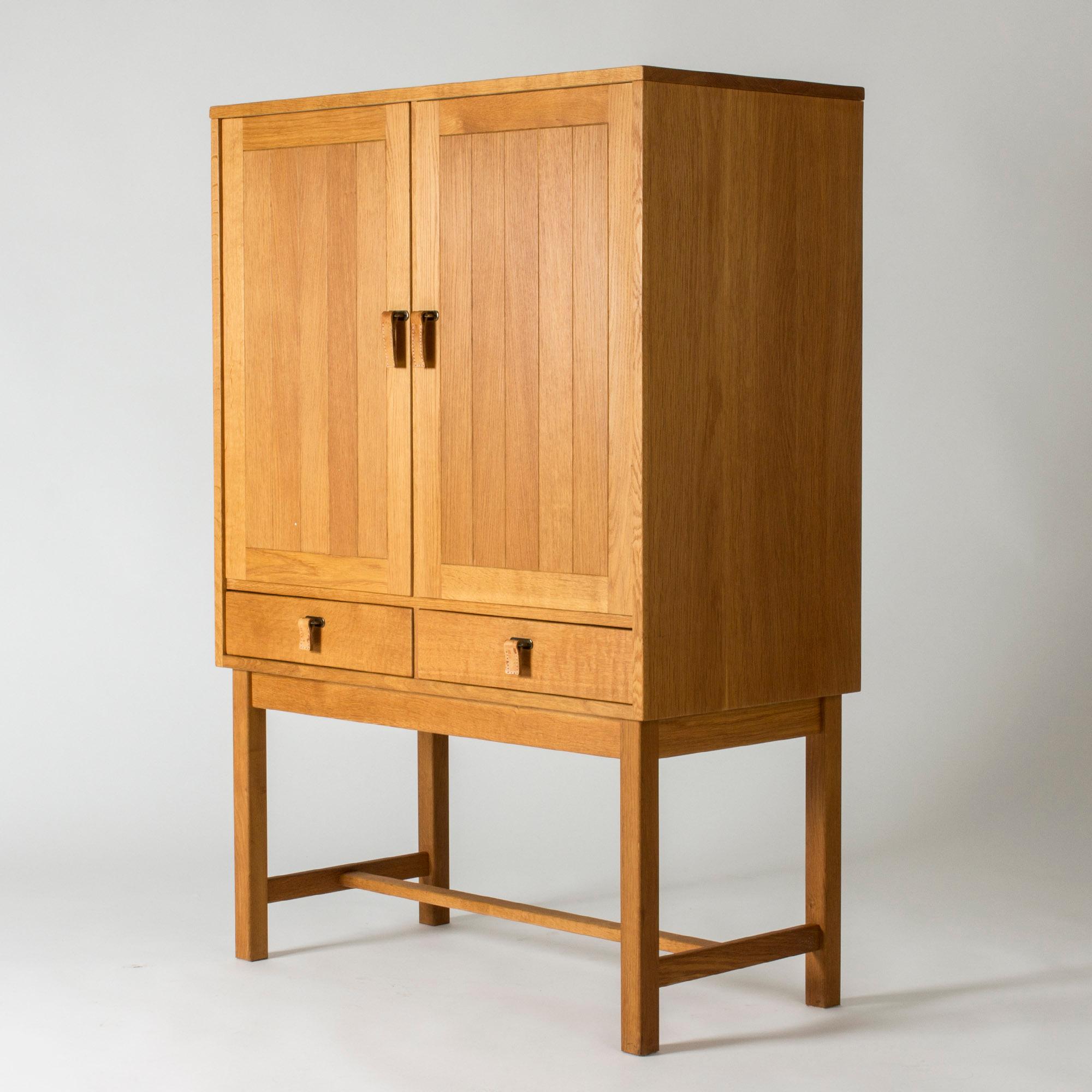 Cool oak cabinet by Kurt Østervig, in a neat size and with a timeless look. Strict lines, decor of embossed stripes on the fronts. Very nice leather strap handles with decorative white seams.