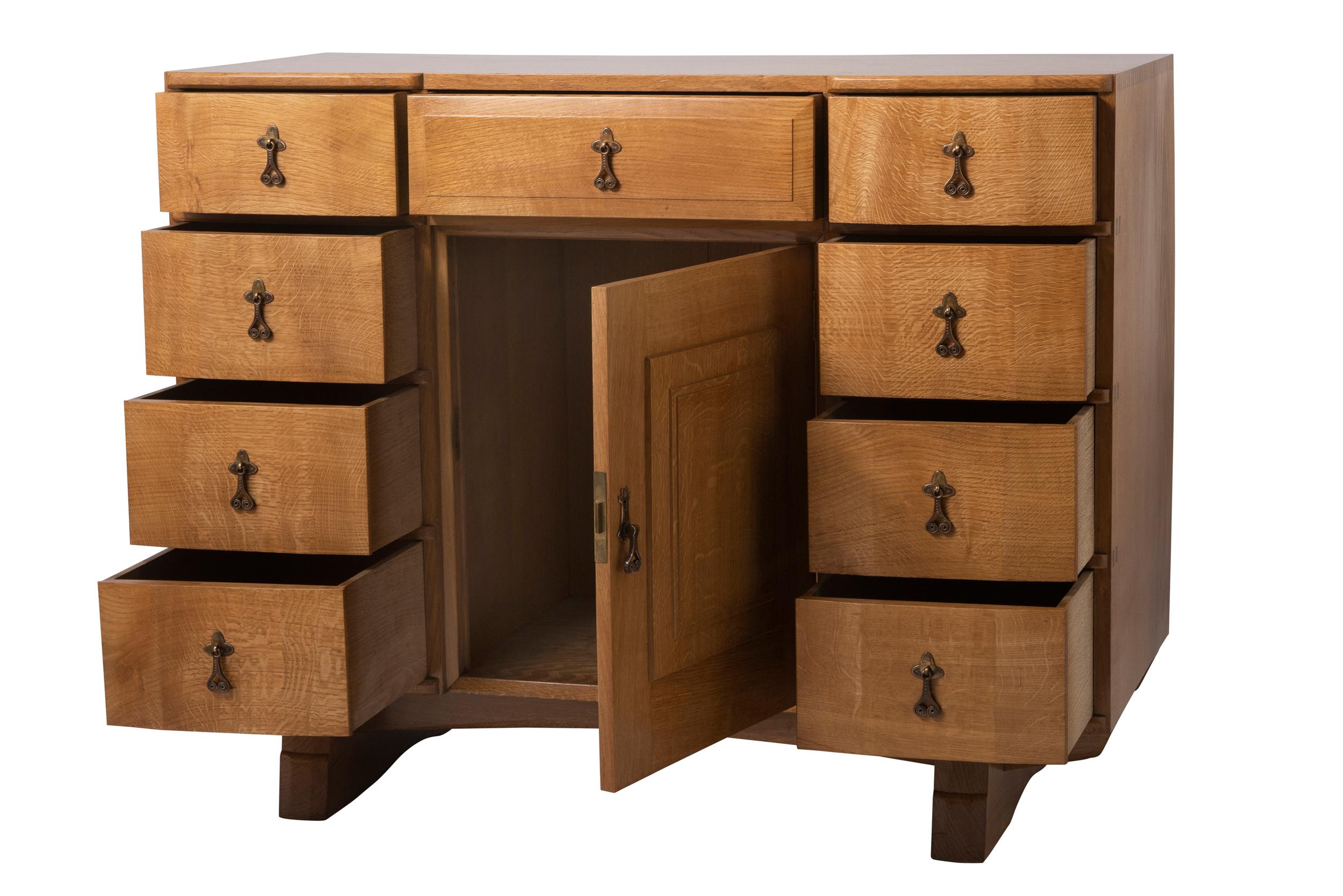 An oak cabinet by Peter Waals (1870-1937)
The shaped top centred with a projecting chamfered drawer, 4 drawers either side of shaped convex form and panelled cupboard beneath.
With beautiful wrought iron scroll handles with chased decoration.
On