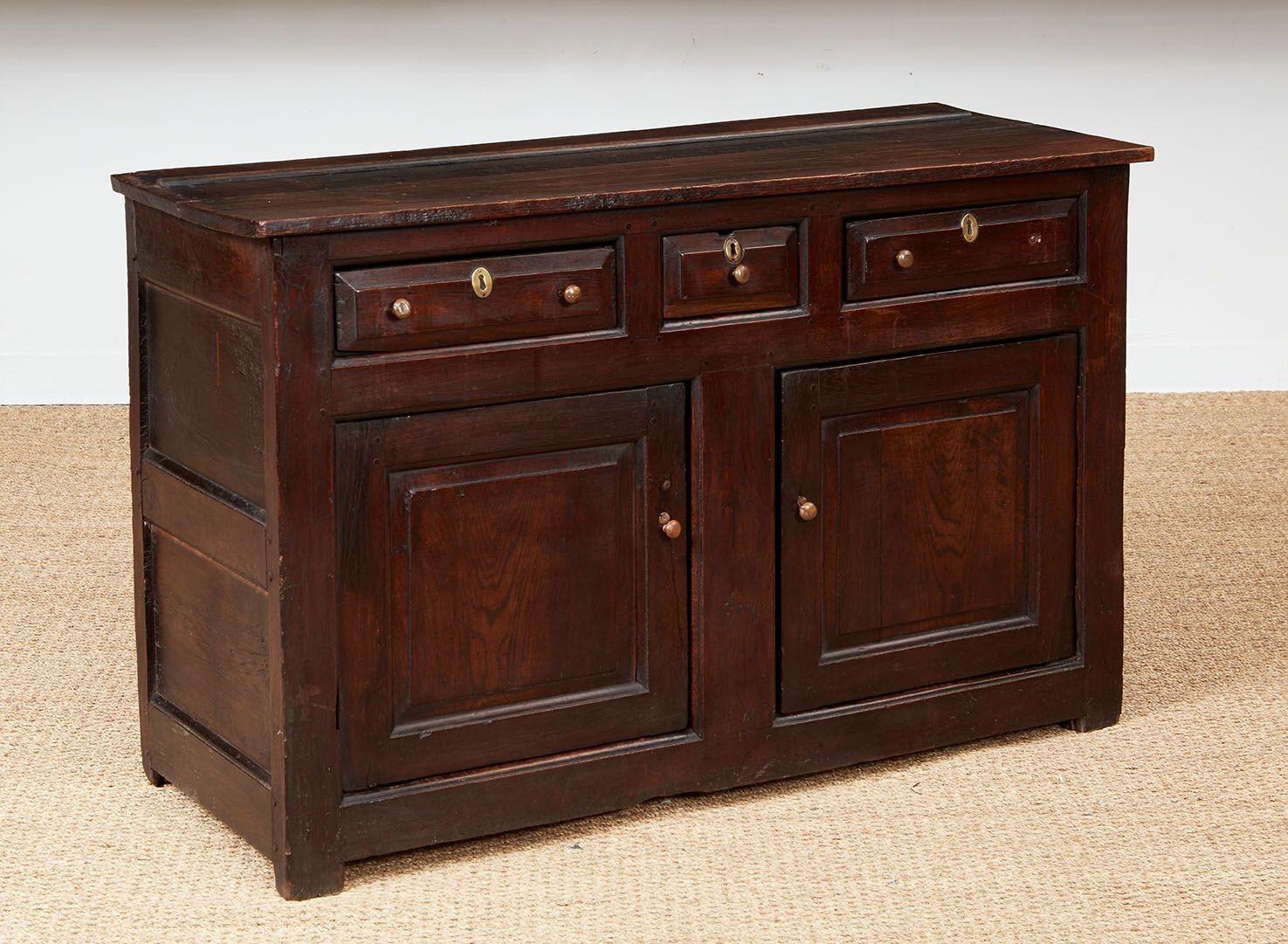 Credenza inglese del 1720 circa con tre cassetti e due ante con stile centrale e ripiano interno.  Costruito con spesse lastre di rovere inglese scuro segate a mano, con pannelli flottanti sulle ante e sui lati e profonde smussature sui cassetti.  