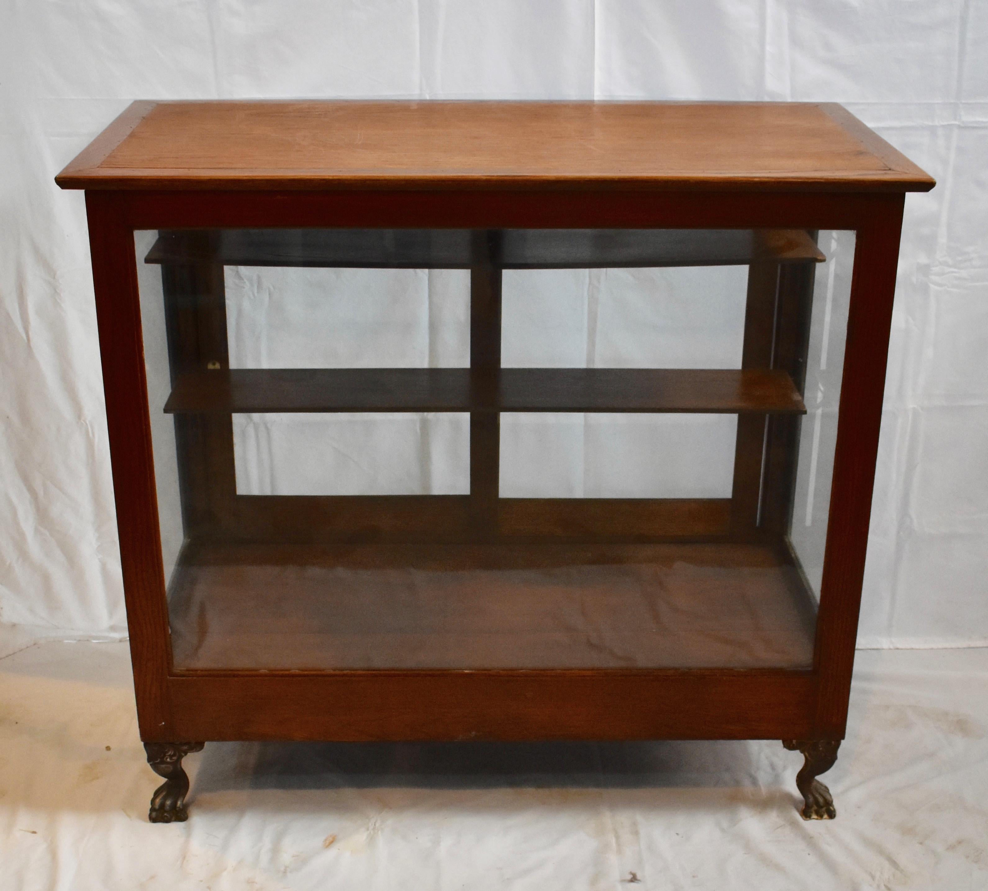 This oak store show case features sliding glass rear doors which allow access to two original adjustable shelves. The front of the cabinet is supported by a pair of unusual cast iron paw feet.