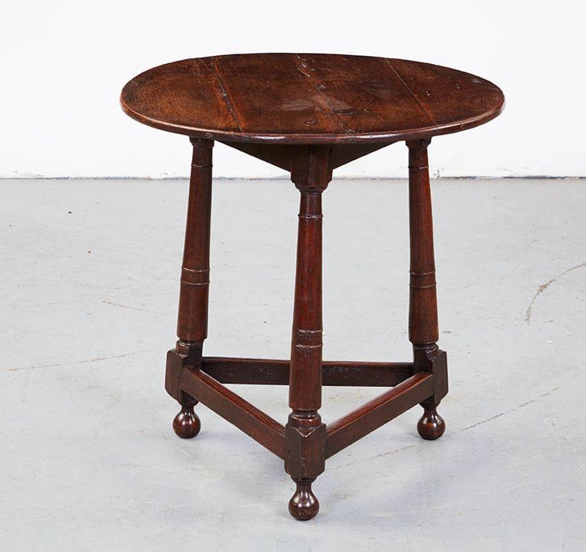 A round, three-legged cricket table in oak having distinctive 'cannon barrel' turned legs joined by low stretchers above ball feet. Good patina and color. English, circa 1780. Attractive and useful as a side table next to a sofa.
 