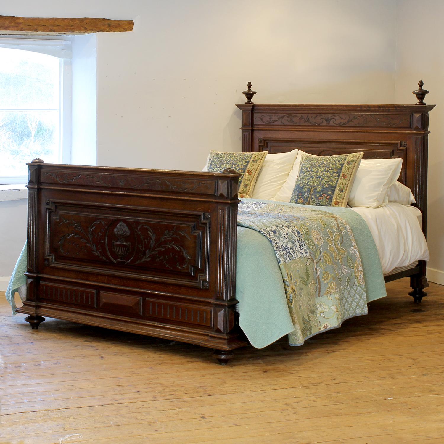 An elaborately carved oak French bed in the Henry II style from the late Nineteenth century, with decoratively carved finials and central carved feature on the head and foot panels depicting urns.

This bed accepts a US Queen Size (or UK King Size),