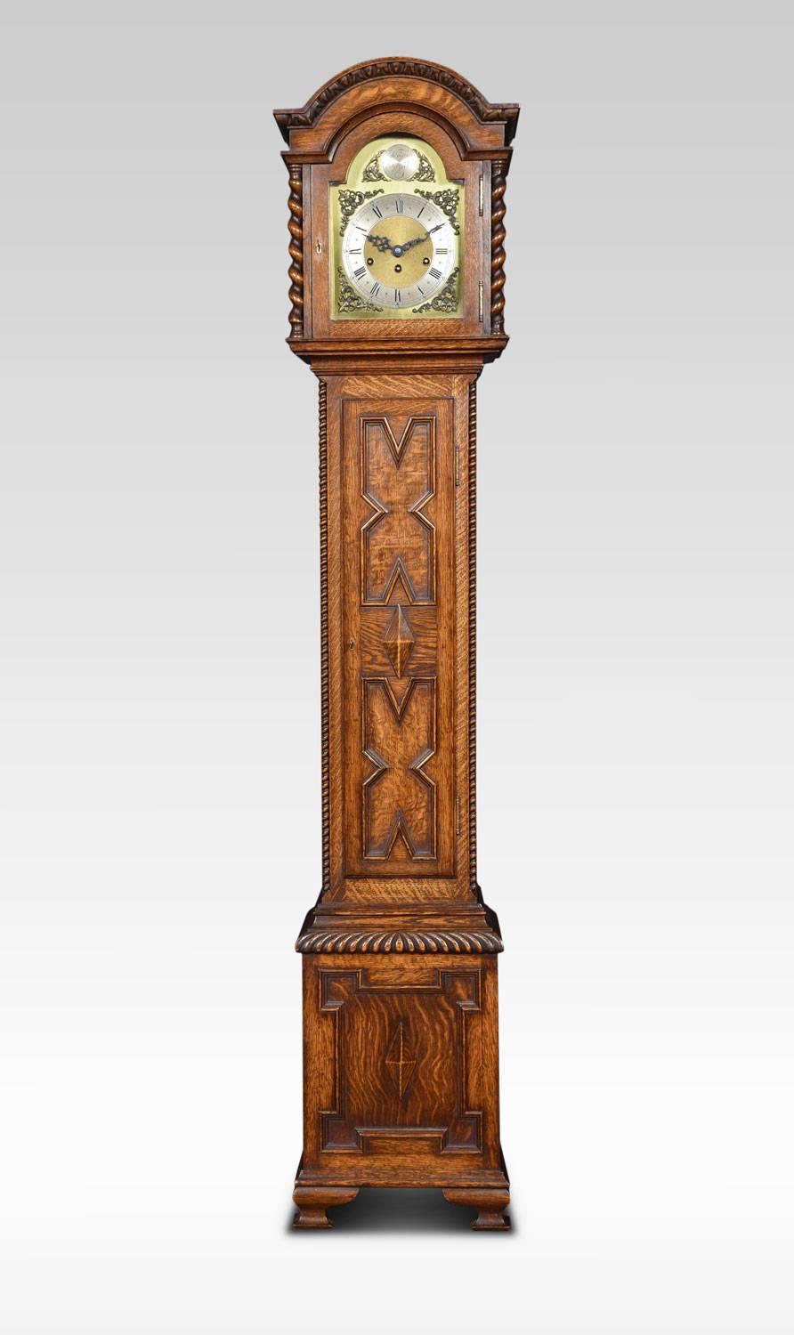 Oak cased grandmother clock, the three train movement by Junghans, the silvered chapter ring with Roman and Arabic numerals, with scroll and floral cast spandrel mounted corners. Striking on eight gongs. The arched hood flanked by twisting columns,