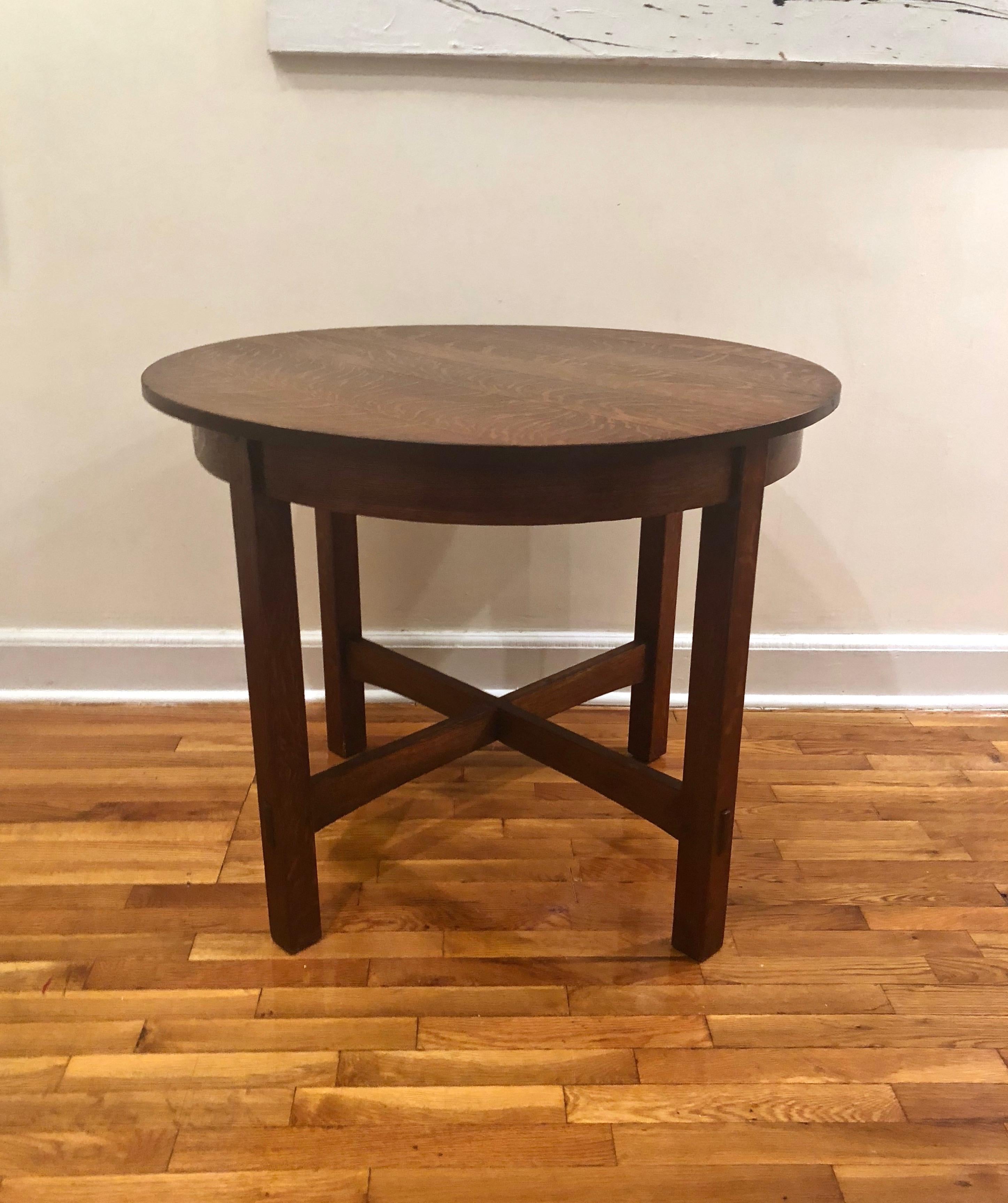 Stickley Arts & Crafts round dining or center table in tiger oak with a x-shaped stretcher on the bottom.