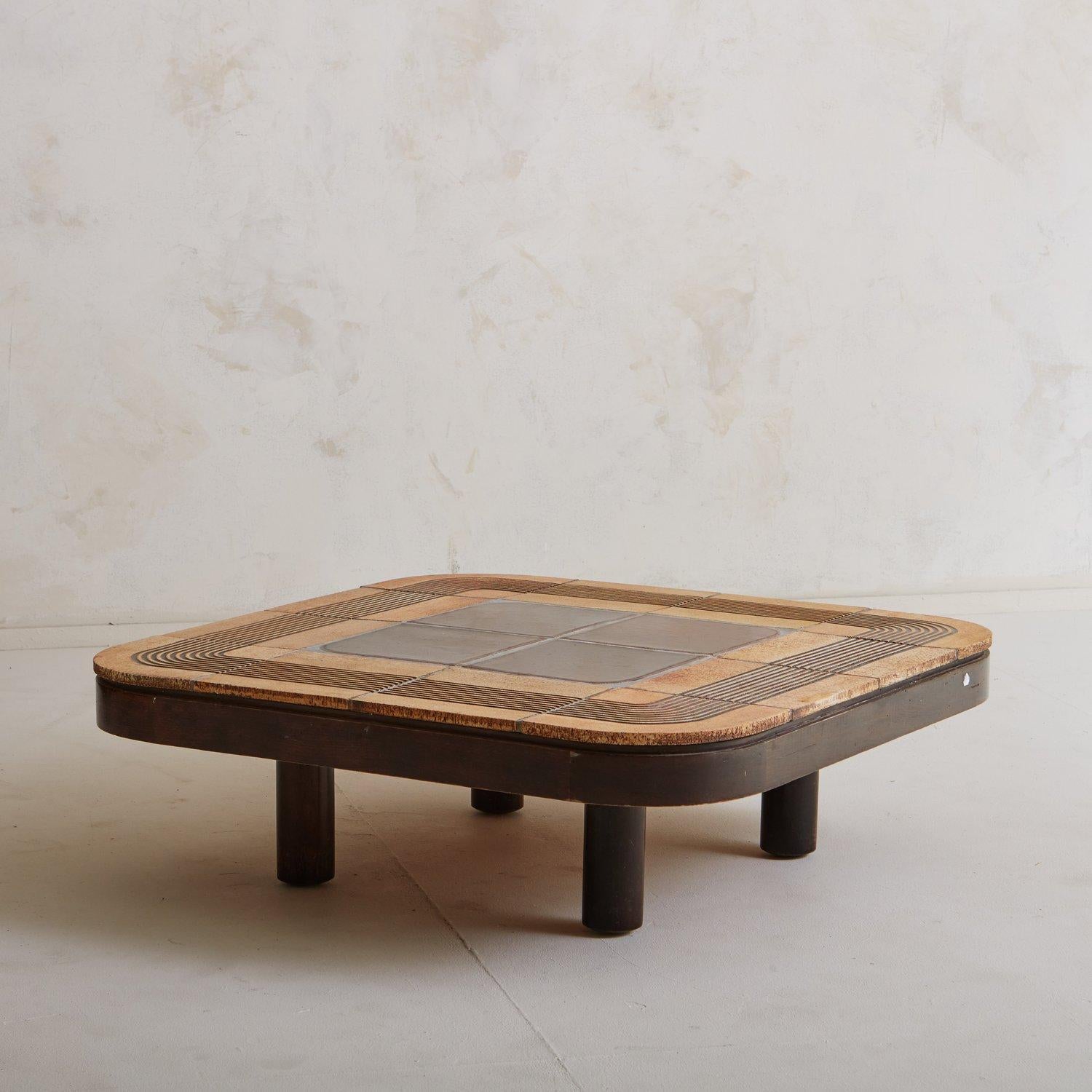 A beautiful French stained oak coffee table by Roger Capron. This table has rounded corners and features ceramic tiles from Vallauris, France in a geometric design with an incised line pattern. It stands on four thick cylindrical legs and has a