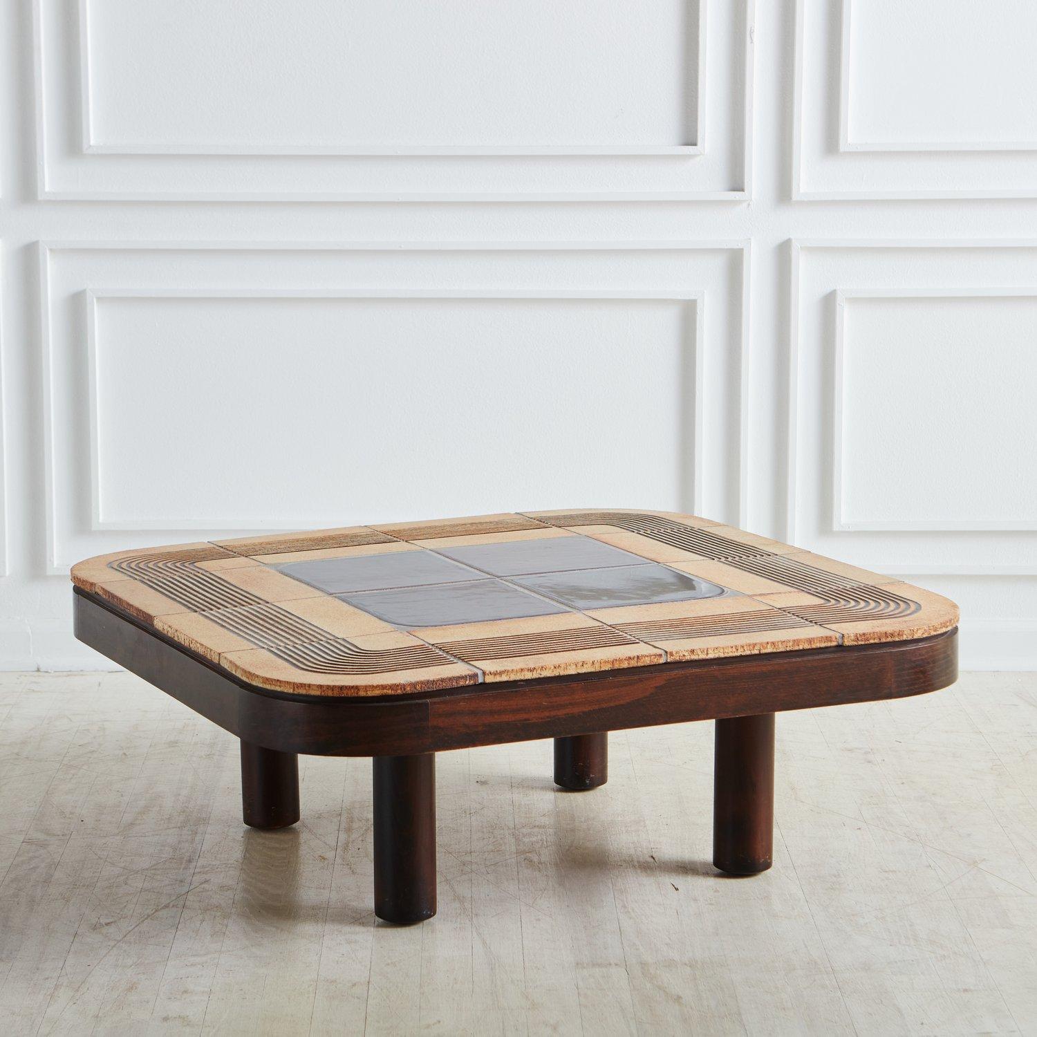 A beautiful French stained oak coffee table by Roger Capron. This table has rounded corners and features ceramic tiles from Vallauris, France in a geometric design with an incised line pattern. It stands on four thick cylindrical legs and has a