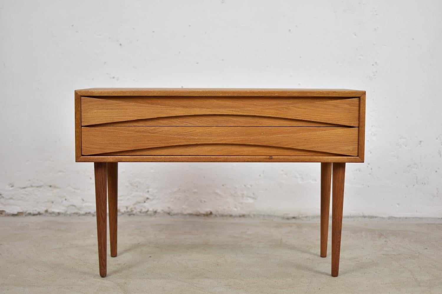Lovely chest of drawers by Niels Clausen for NC Möbler, Denmark, 1960s. Often presented in teak or rosewood, our chest is made out of oak. Two drawers with scalloped pulls and solid tapered legs. Professionally restored. Rare. Often misattributed to