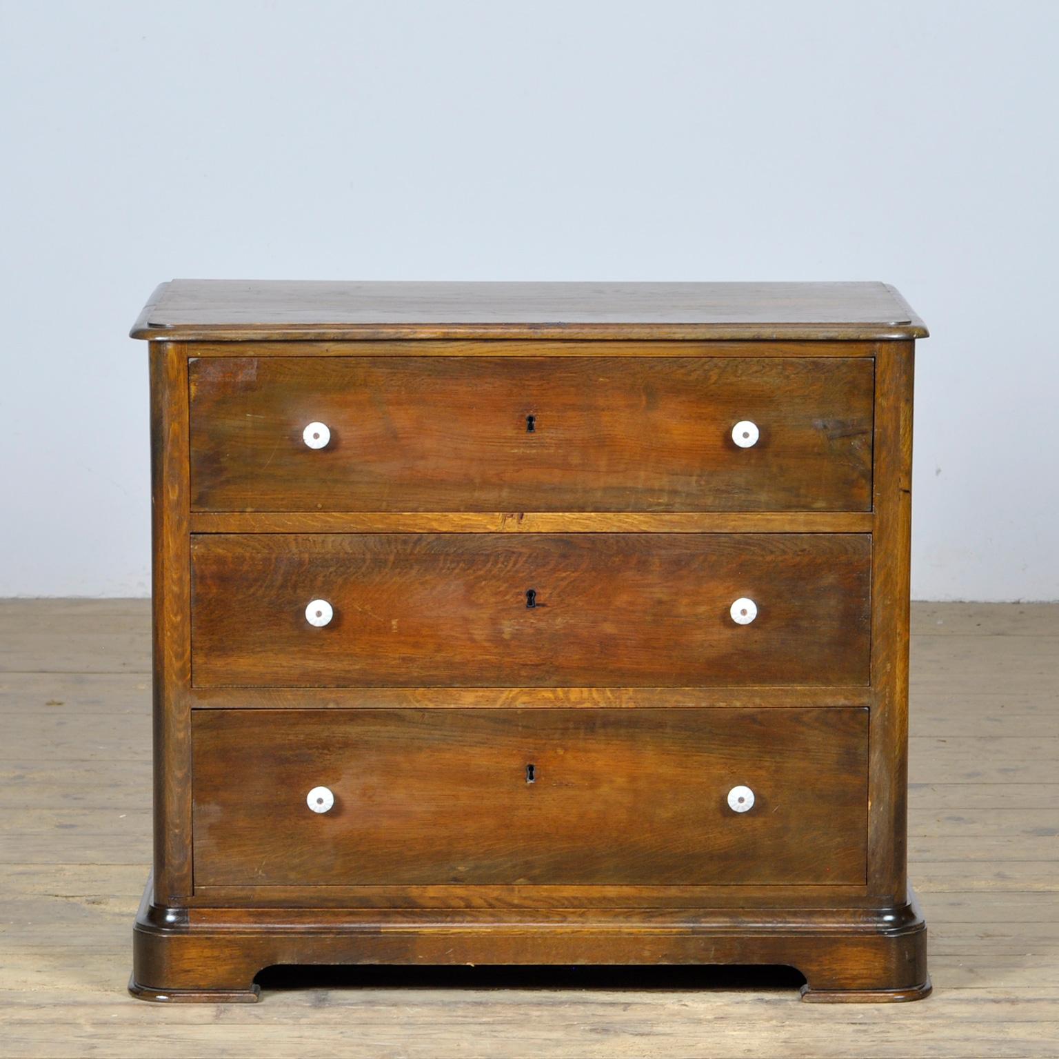 A beautiful antique oak and pine chest of drawers from around 1920. The chest of drawers has 3 drawers, the bottom of which is higher. The drawers are made with dovetail joints and fitted with porcelain knobs. The chest of drawers stands on rounded