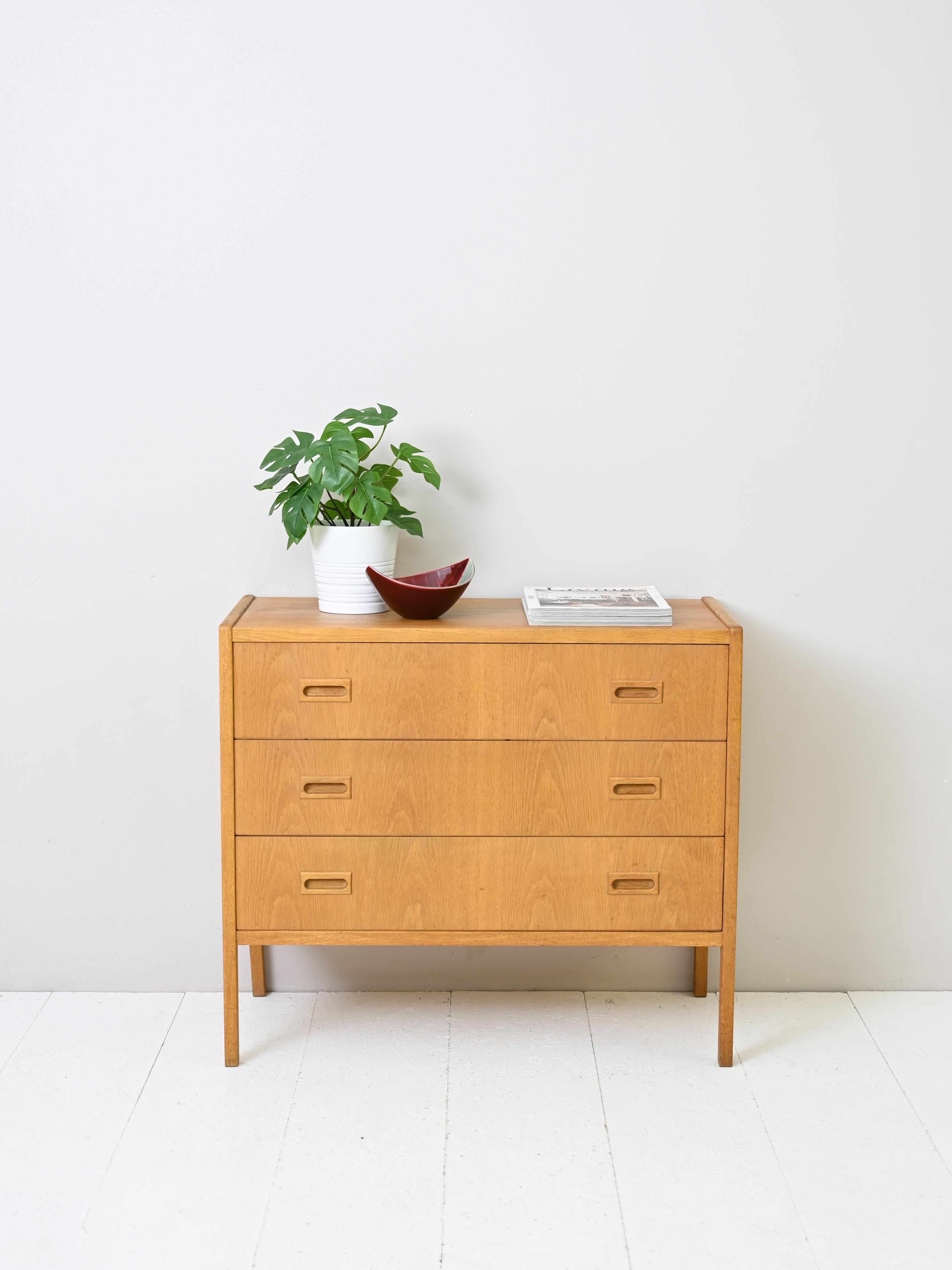 Vintage cabinet with three drawers of Scandinavian manufacture produced in the 1960s.
Simple, linear forms for this chest of drawers in warm teak wood tones.
Clean lines and drawer handles carved from wood are the hallmarks that
hark back to