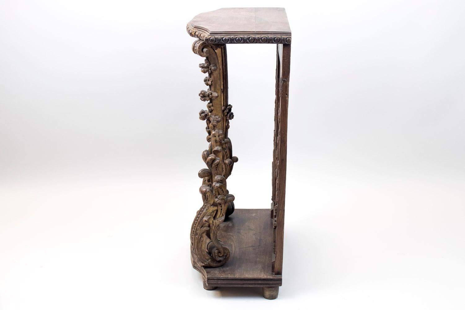 Small natural oak console-stand, composed of 18th century elements assembled during the 19th century. It standings on four small cylindrical legs supporting a molded chantourné tray. On top, two finely carved uprights decorated with swirls, acanthus
