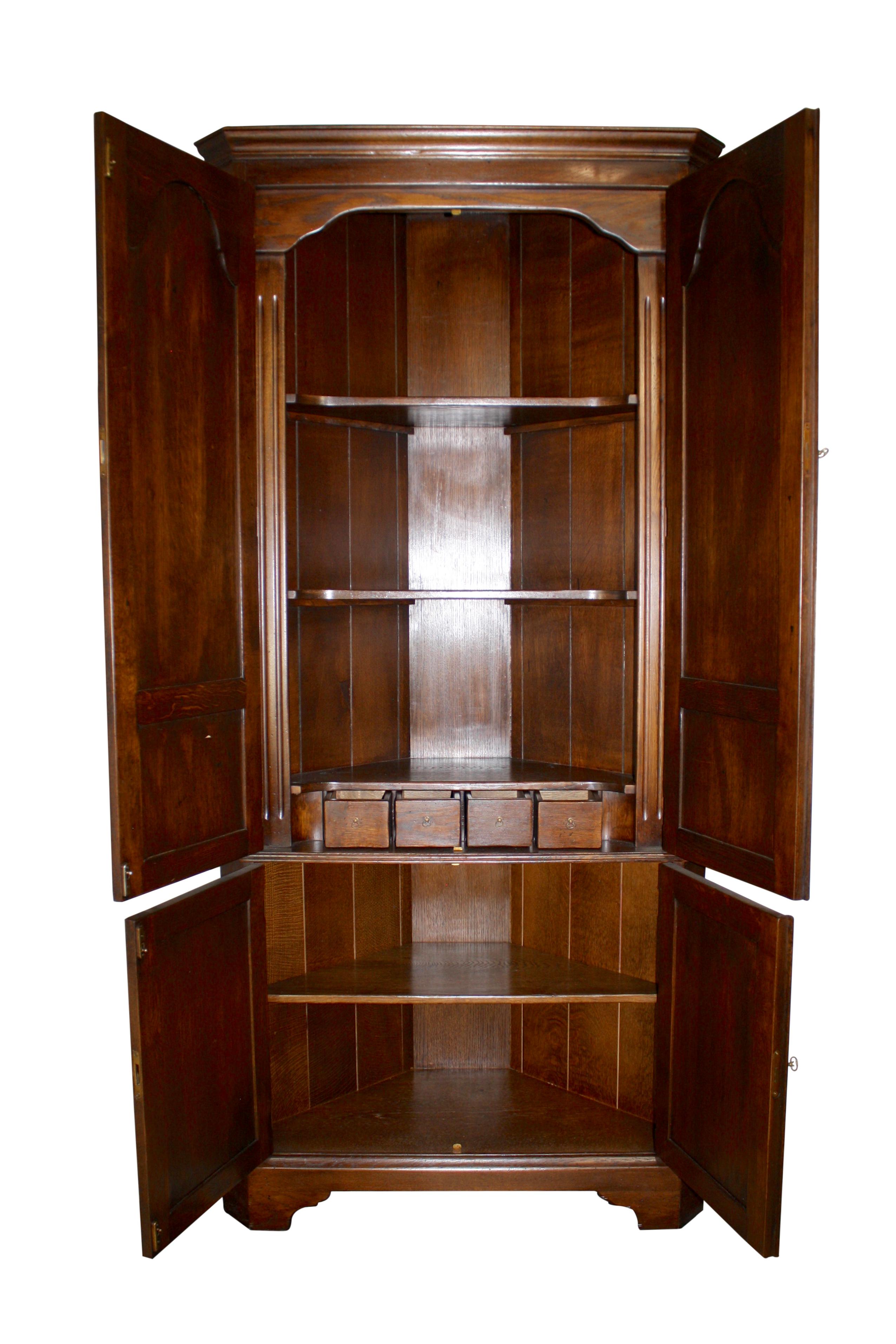 Two sets of doors open to substantial storage in this oak corner cabinet. The top set features tall, cathedral raised panels over small, rectangular raised panels. These doors open to two shelves and four small drawers with ring pulls. The bottom