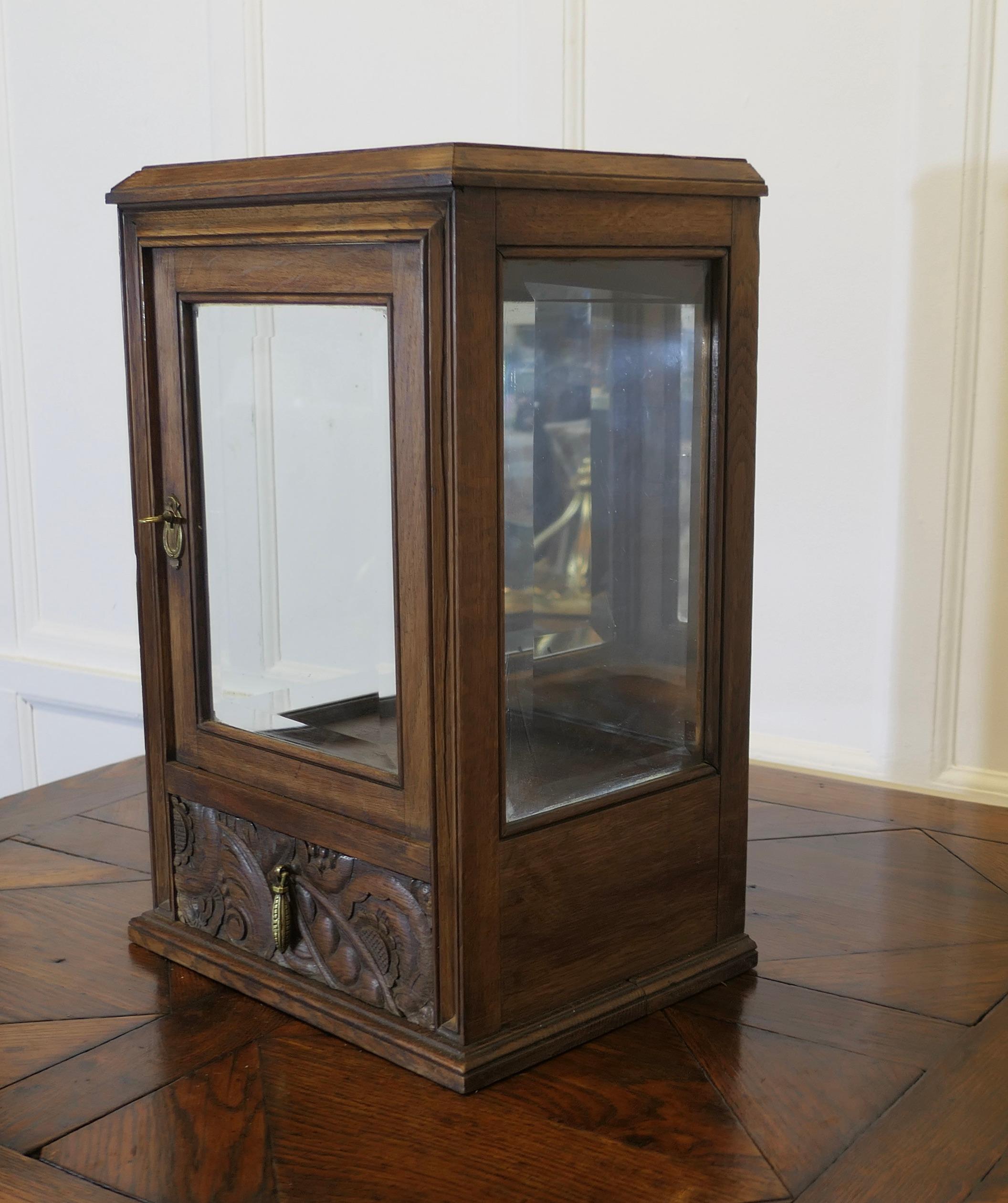 Oak Counter top Display Cabinet with Drawer

A useful little cabinet, it has 3 bevel cut glass sides and in interior mirror at the back so the contents can be viewed well from all sides. At the bottom there is a small drawer with a carved front
All