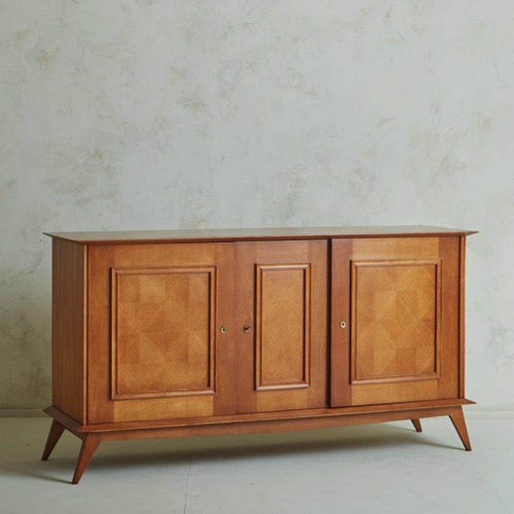 A 1940s French credenza in the style of Jules Leleu. This piece was constructed with beautifully grained oak wood and has three doors which feature cornice detailing and a stunning parquetry inlay. The doors have patinated brass hardware and open to