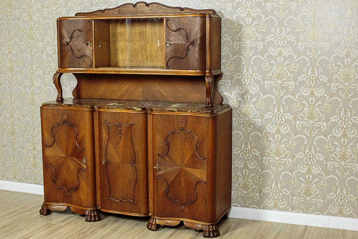 A piece of furniture circa 1935, made in oak, and softwood in oaken veneer.
This cupboard is composed of a three-door base, and a removable, three-door setting with a glazed middle.
Furthermore, the whole is supported on prominent legs in the