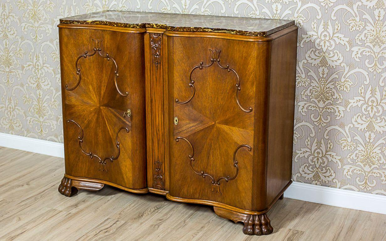 A sideboard circa 1935, made in oak and softwood with oaken burl.
Furthermore, the whole is two-door and supported on prominent legs in the shape of paws.
The upper section of this piece of furniture has a marble top, which concave-convex shape is