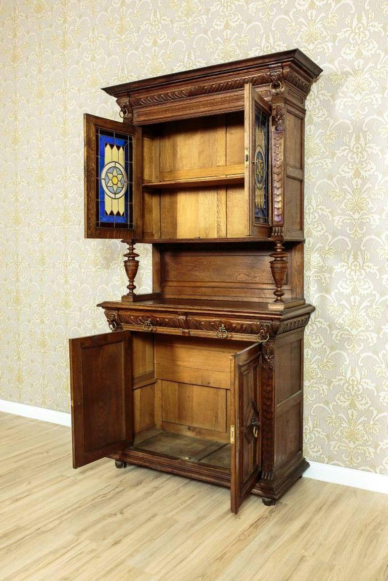 A decorative cupboard made in oakwood, circa 1910.
This piece of furniture is composed of two segments: a two-door base and an upper section.
The door panels of the upper section with beautiful stained glass with geometrizing motifs.
The whole is