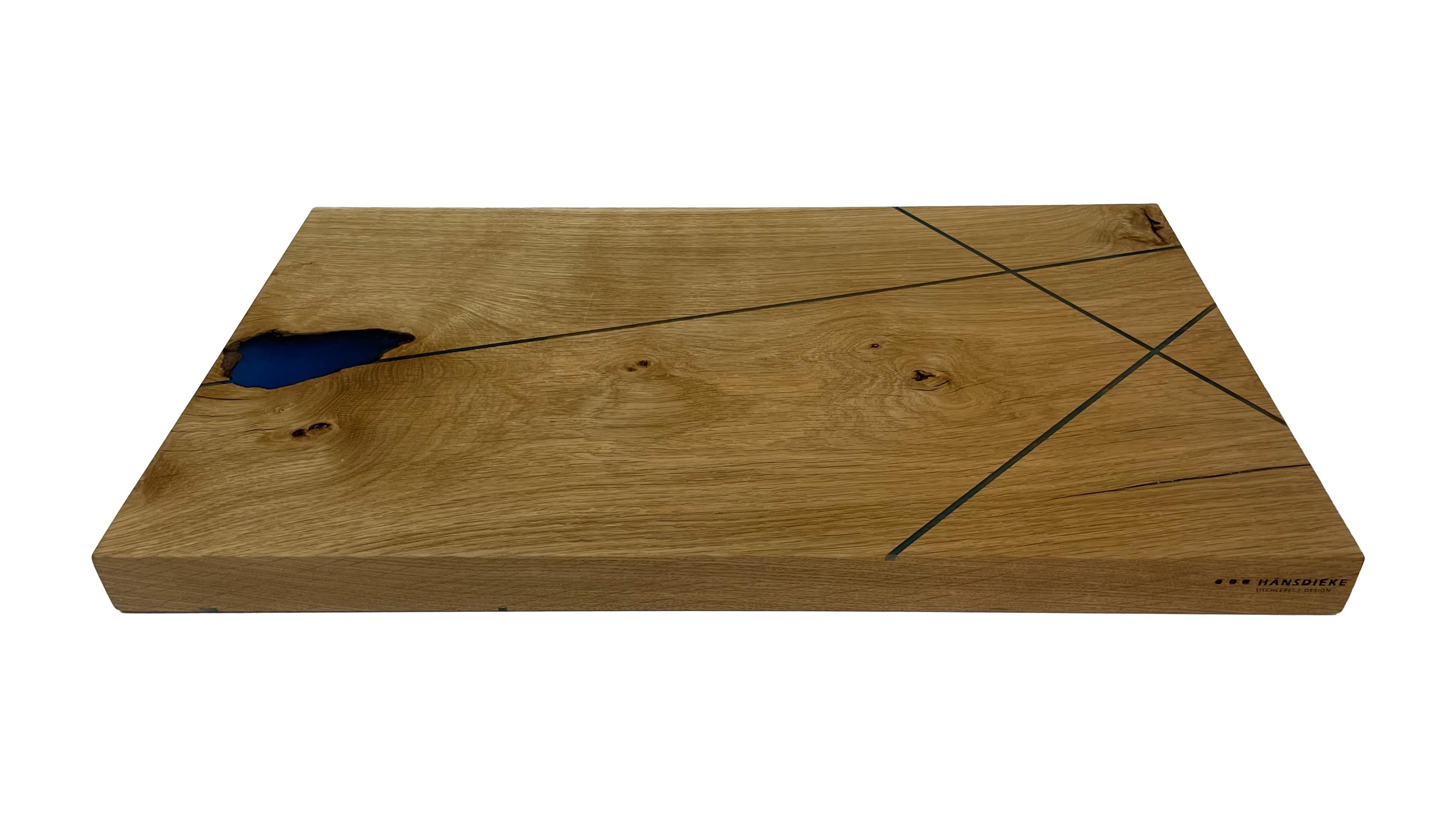 The oak cutting board was glued in multiple layers and cracks, knots, etc. were filled with high-quality epoxy. As a small design, fine lines were also grooved and filled with epoxy resin. The surfaces are very finely ground and sealed with oil. The