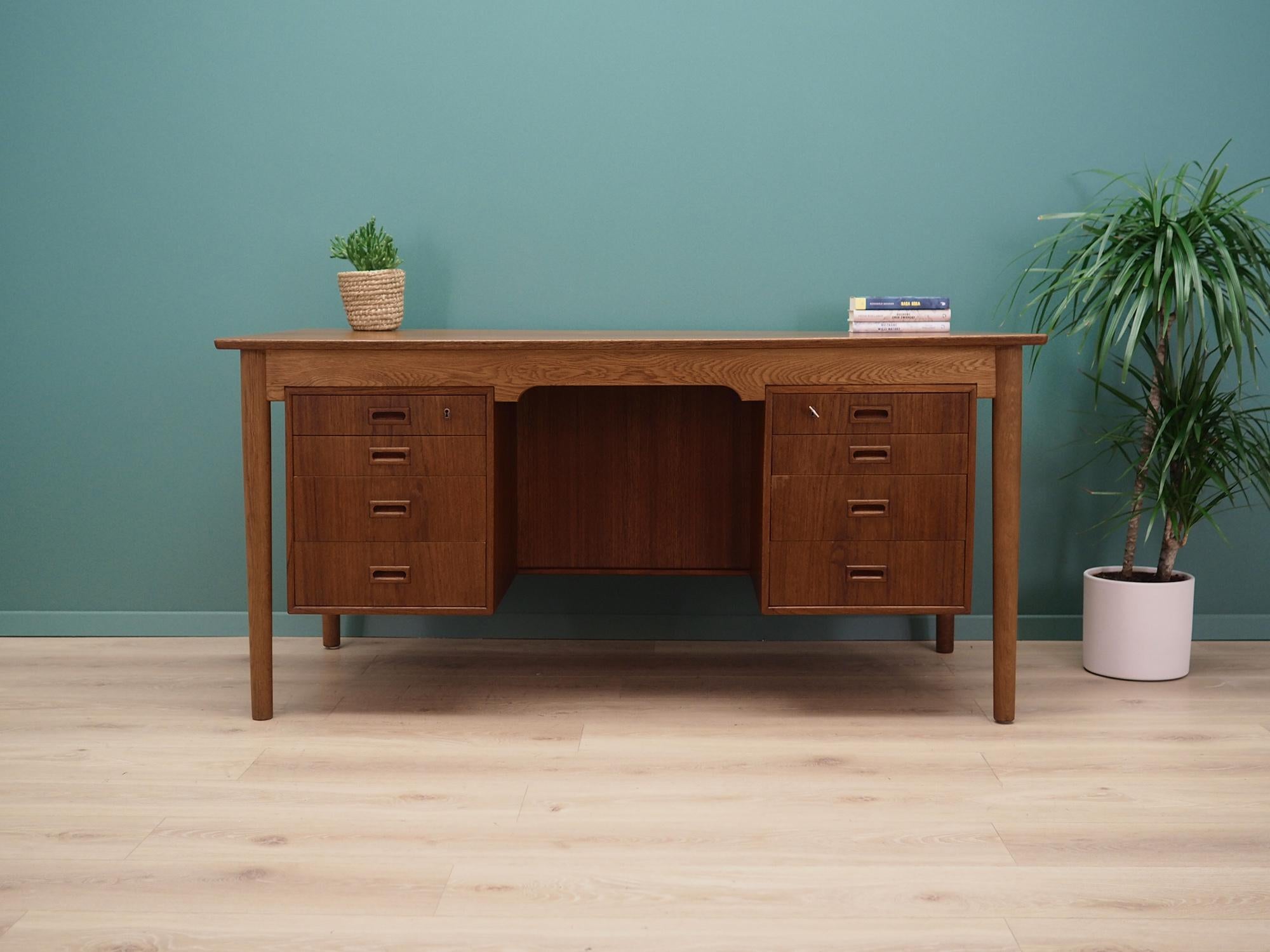 Desk made in the 1970s, Danish production.

The structure and top are covered with teak veneer. The legs are made of solid oak wood, perfectly integrated into the structure of the desk. The surface after refreshing. The front of the desk has eight