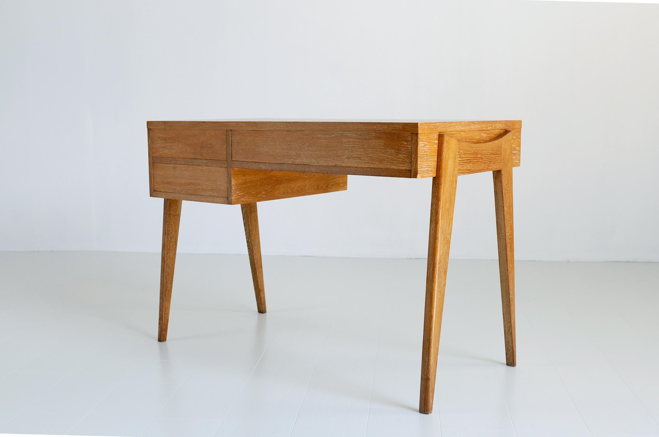 Oak desk with three drawers, French Reconstruction 1950. Perched on a portico base, the box has a large drawer and two other drawers. The blond oak is ceruse, enhanced by patinated brass handles. Sober, elegant and finished on all sides, this desk