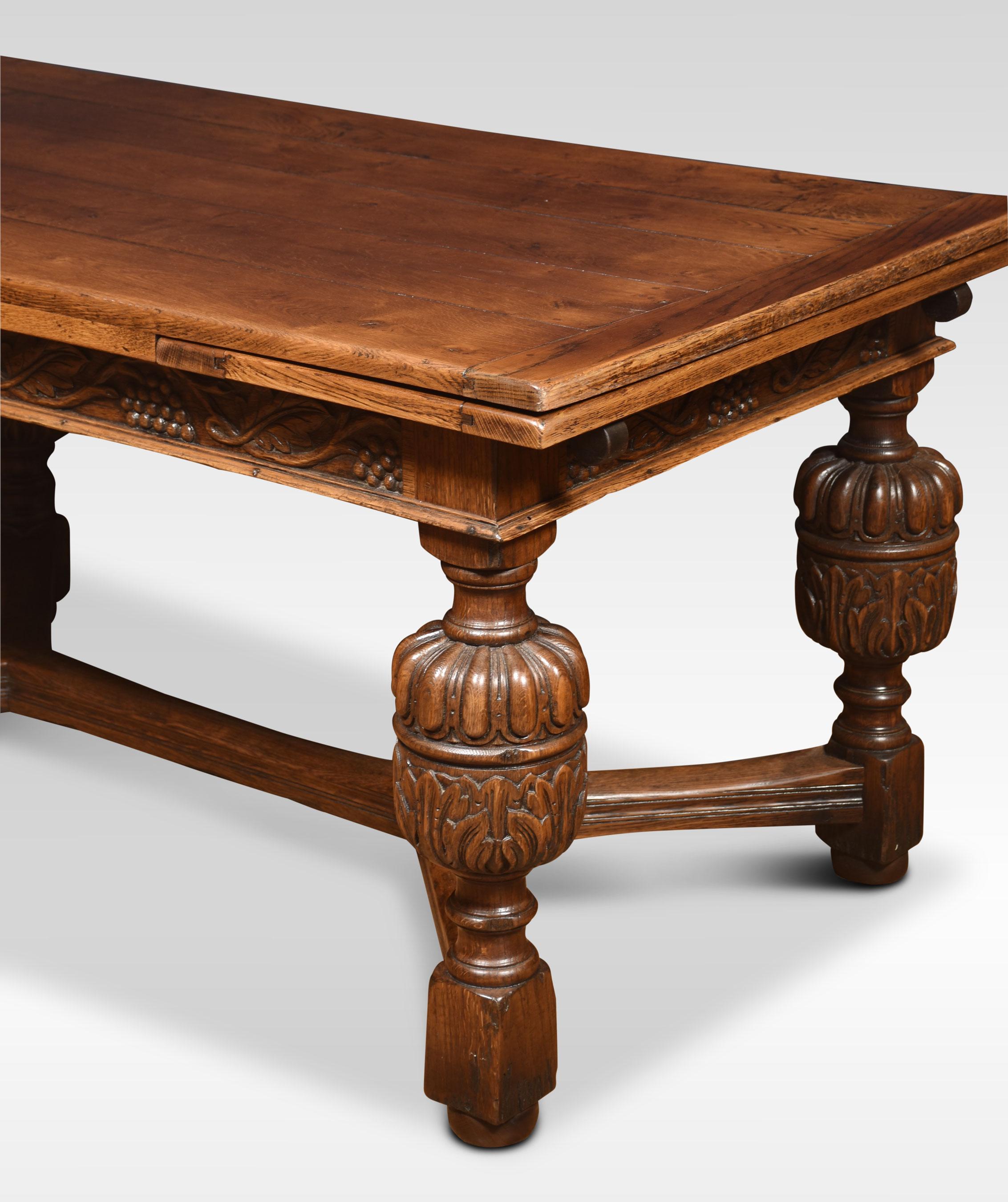 An impressive Elizabethan style oak draw-leaf table. The plank top having pull-out leaves to each end above a strap-work frieze with scrolling foliated carving raised on bulbous cup & cover legs leading down to block feet united by