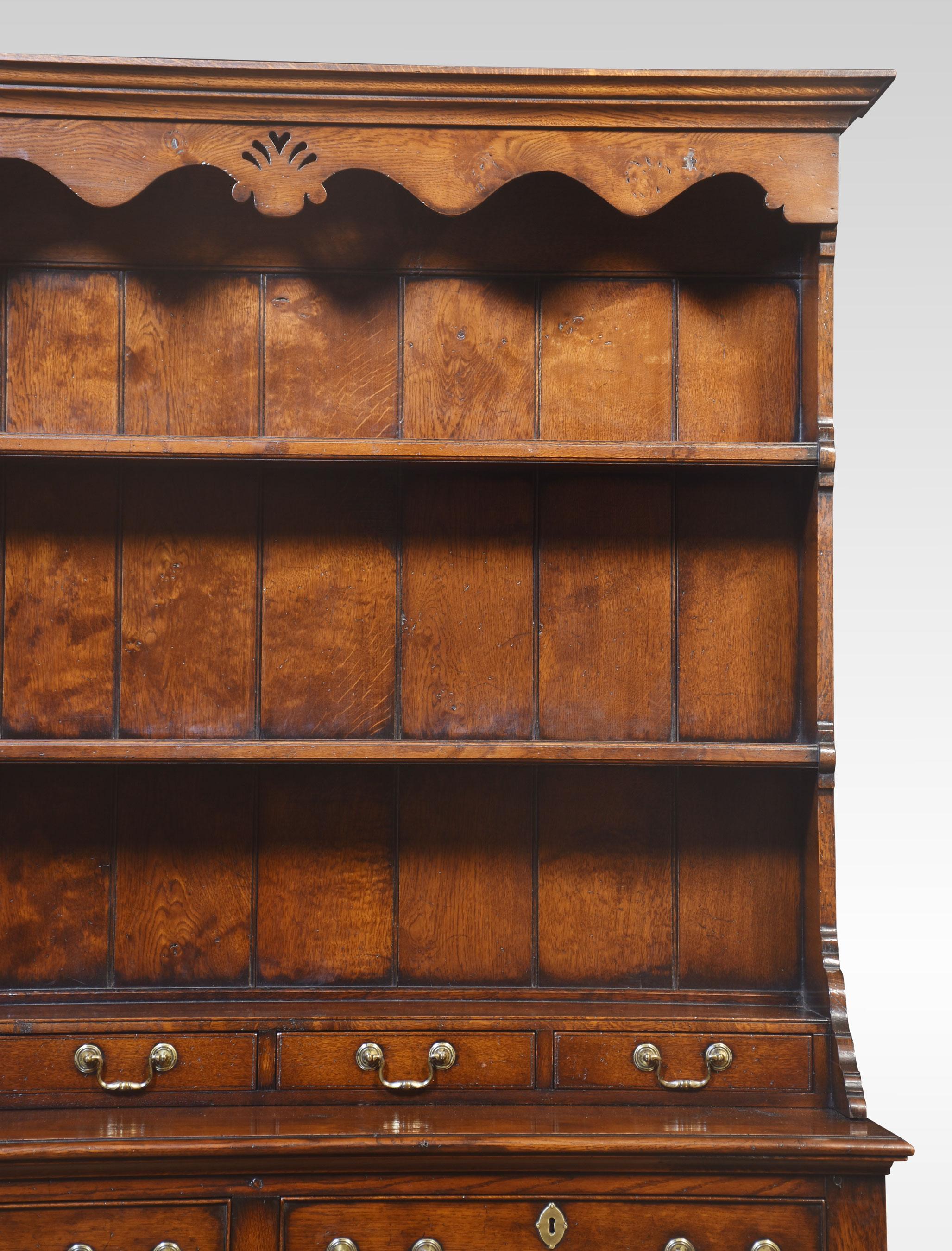 Oak dresser, the top plate rack top with a wavy apron, and two shelves above an assortment of small drawers with brass swan neck handles. The base section having two large drawers above four conforming arched panelled cupboard doors opening to