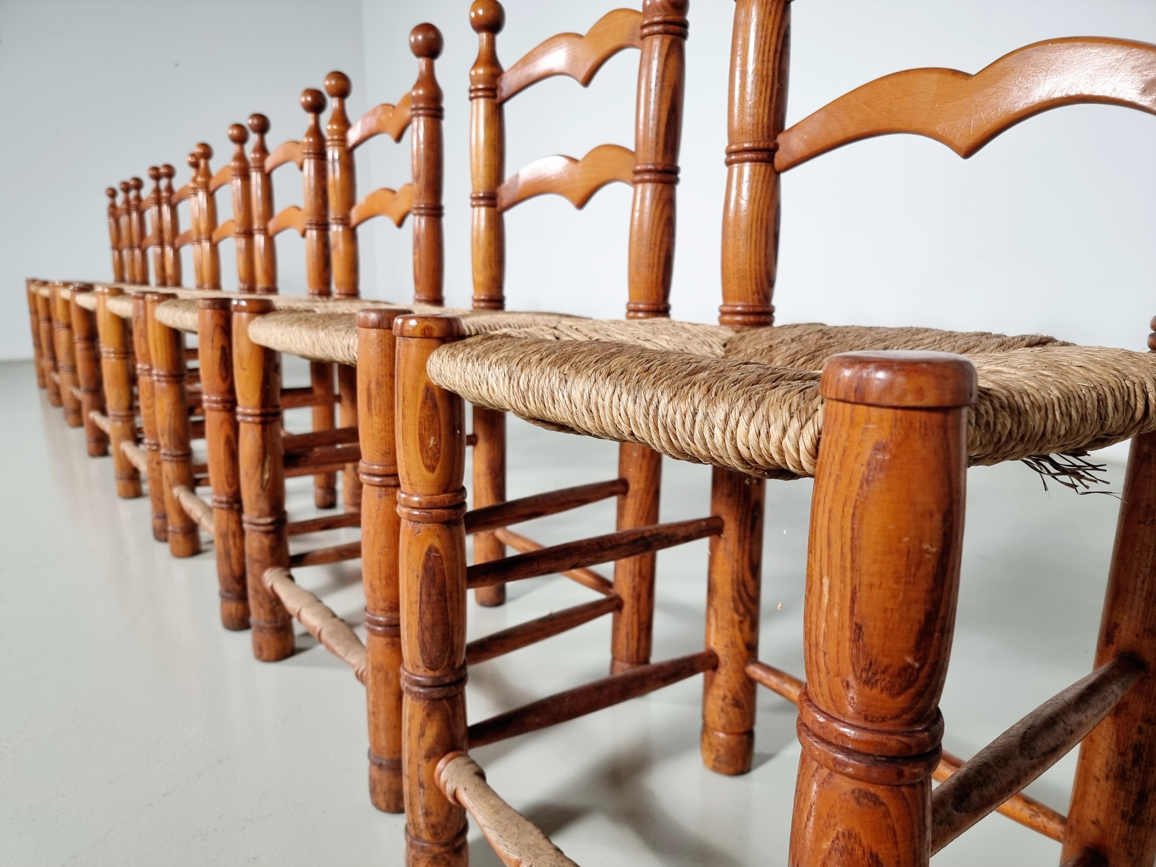 Lot de 12 chaises de salle à manger rustiques de style fermier en chêne avec des sièges en jonc tressé. Fabriquées en France dans les années 1970. Les cadres en chêne sont dans leur finition d'origine légèrement teintée. Les sièges en jonc sont