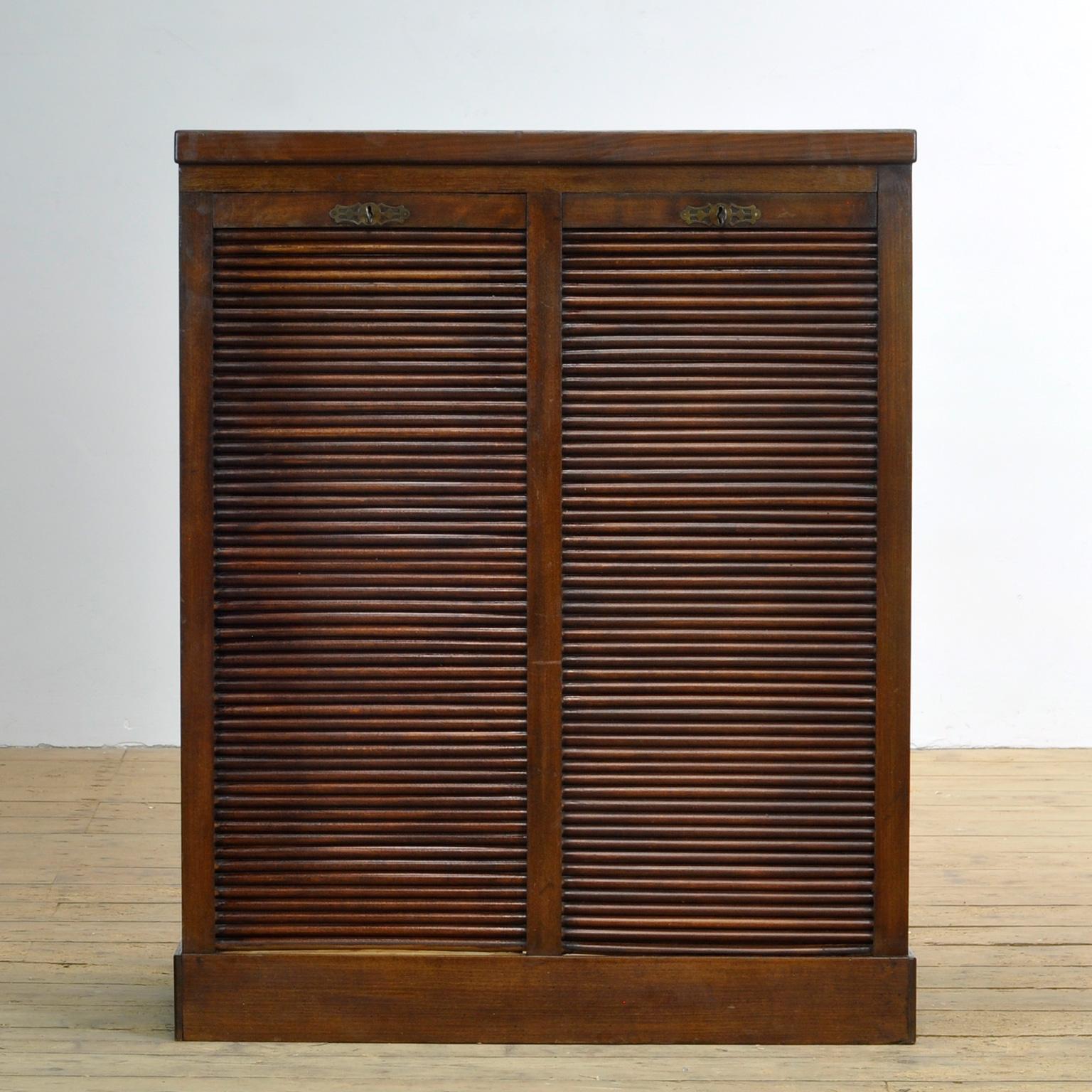 This wooden roller door cabinet / filing cabinet was made from oak in circa 1920. With properly working locks and keys. Behind the 2 roller doors 4 adjustable shelves. Handy for paperwork, for example.