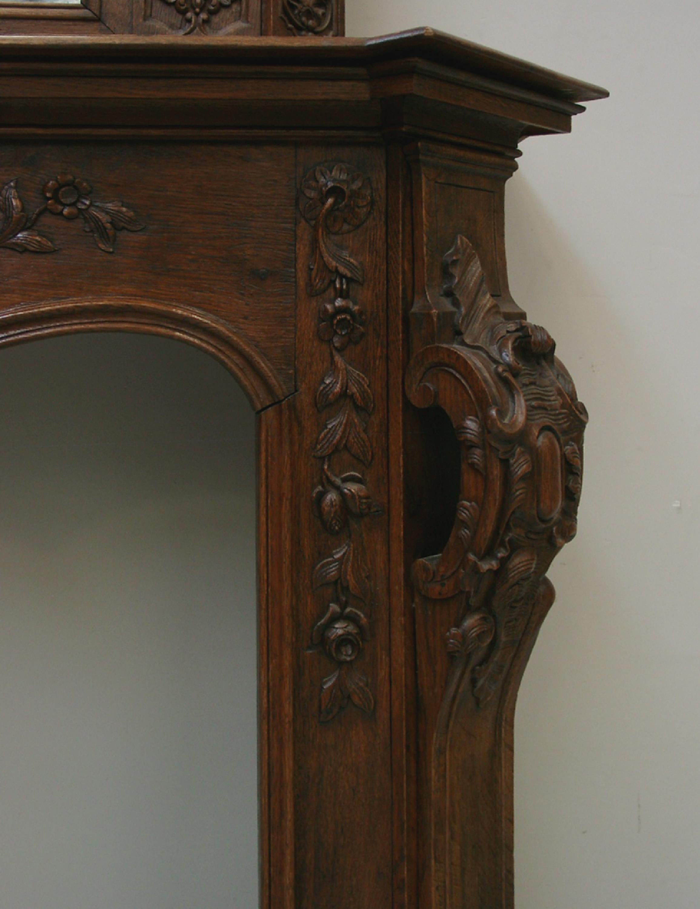 Cheminée en chêne avec miroir en trumeau. Dans un élégant style Louis XV, la cheminée est décorée d'ornements finement sculptés : une coquille centrale est flanquée de guirlandes de fleurs. Les jambages sont décorés de cartouches rococo qui