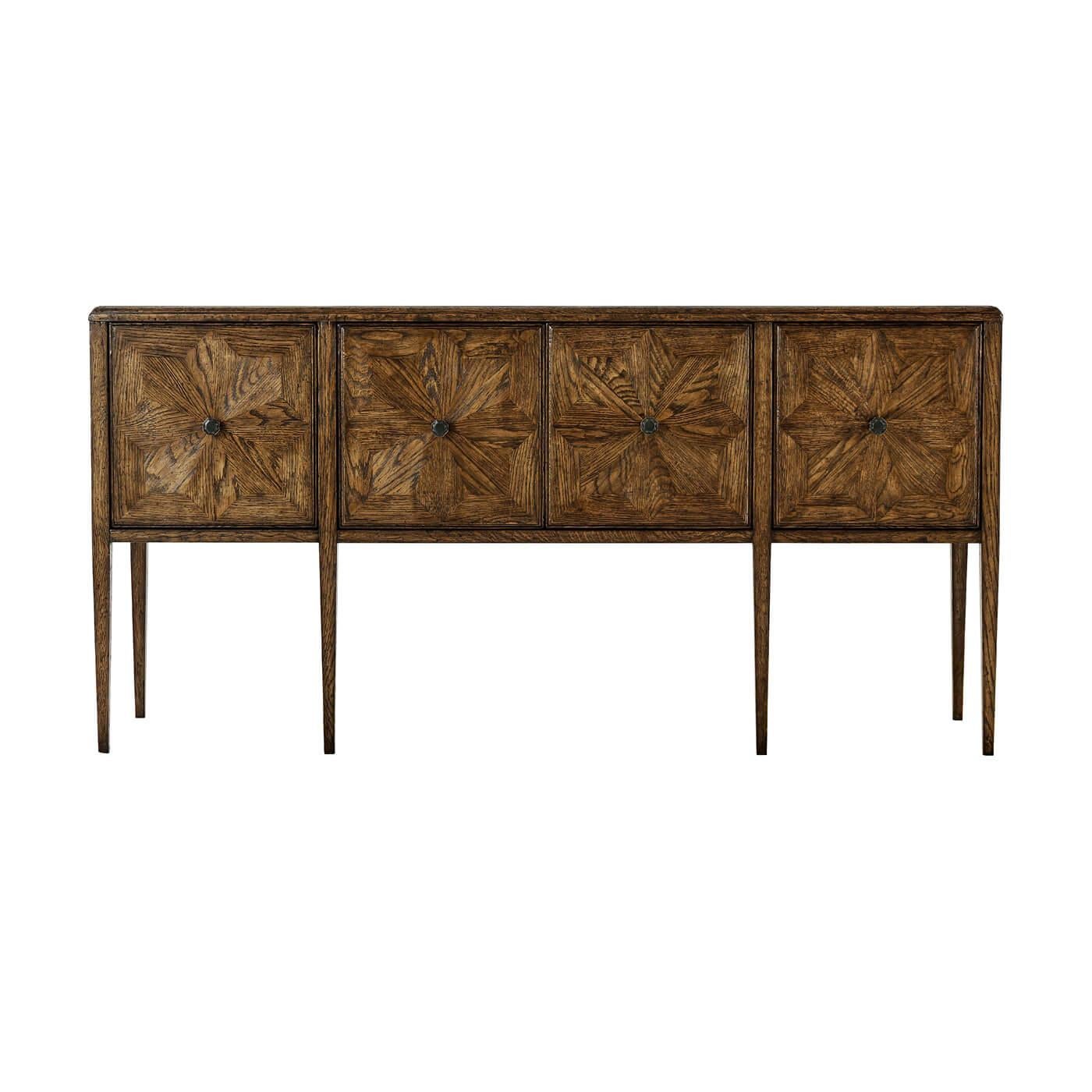 Aparador buffet de cuatro puertas, de roble oscuro, chapado con motivos radiales de estrellas. Sus puertas inspiradas en los mosaicos se acentúan con herrajes en acabado Bronce Verde y se asientan sobre patas cónicas de roble.  Esta sofisticada