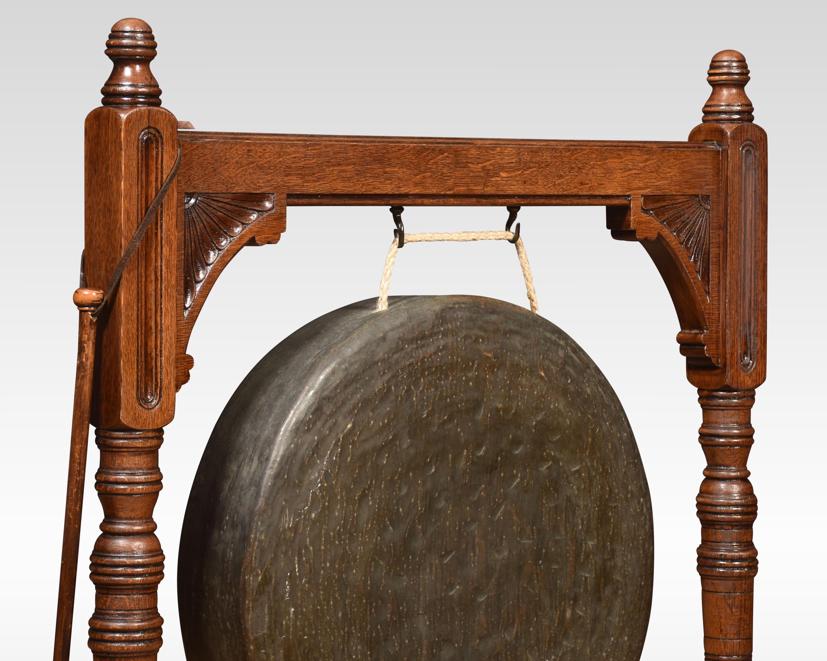 Oak framed floor standing diner gong and beater, the carved top rail, flanked by turned finials raised on ring turned carved pillars and a bobbin turned gallery below, supporting the original brass gong. All raised up on splayed