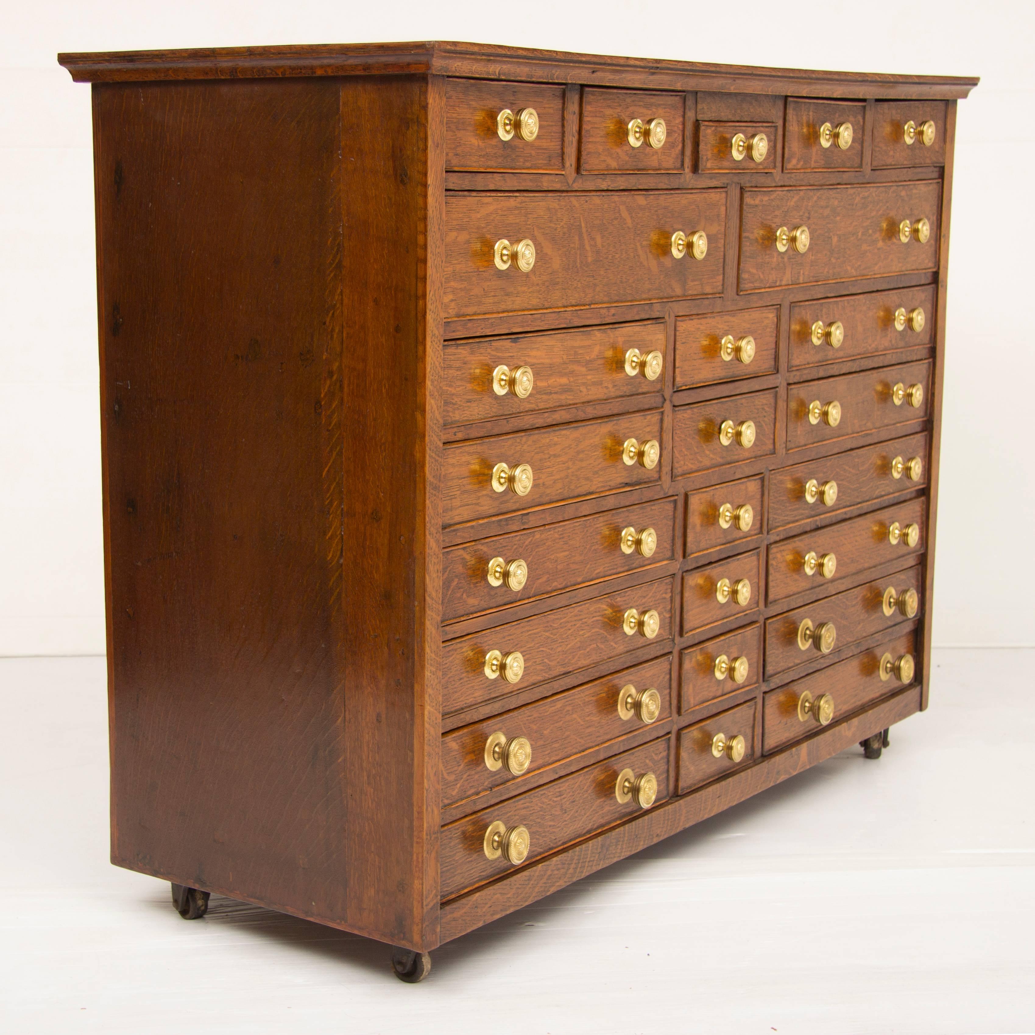 Oak Georgian bank of drawers which was probably on a stand originally and at some point has been put on casters. It has 25 drawers of varying sizes.